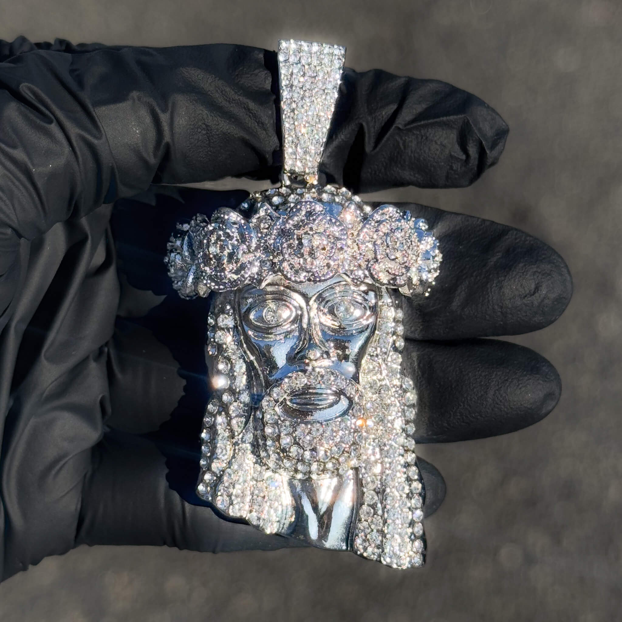 Silver iced-out Jesus crown pendant with rose design and full pavé stones shown in hand.