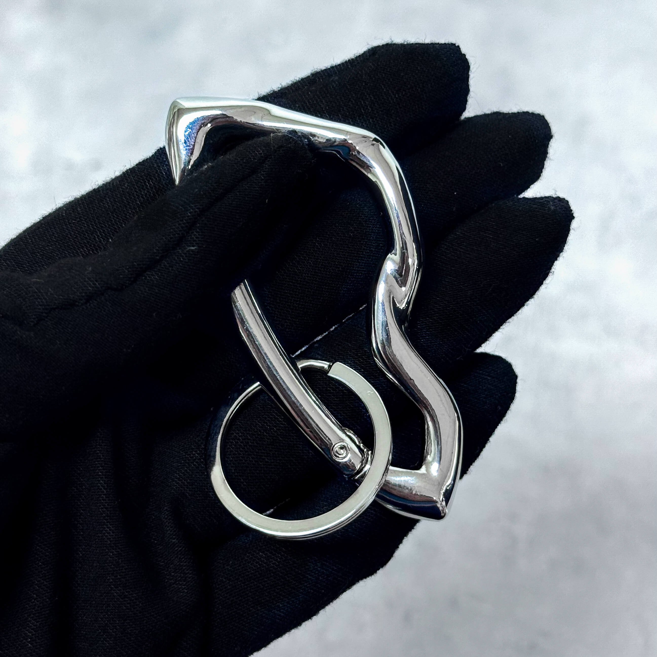 Silver Irregular Y2K carabiner keychain with wavy shape and key ring shown in black-gloved hand.
