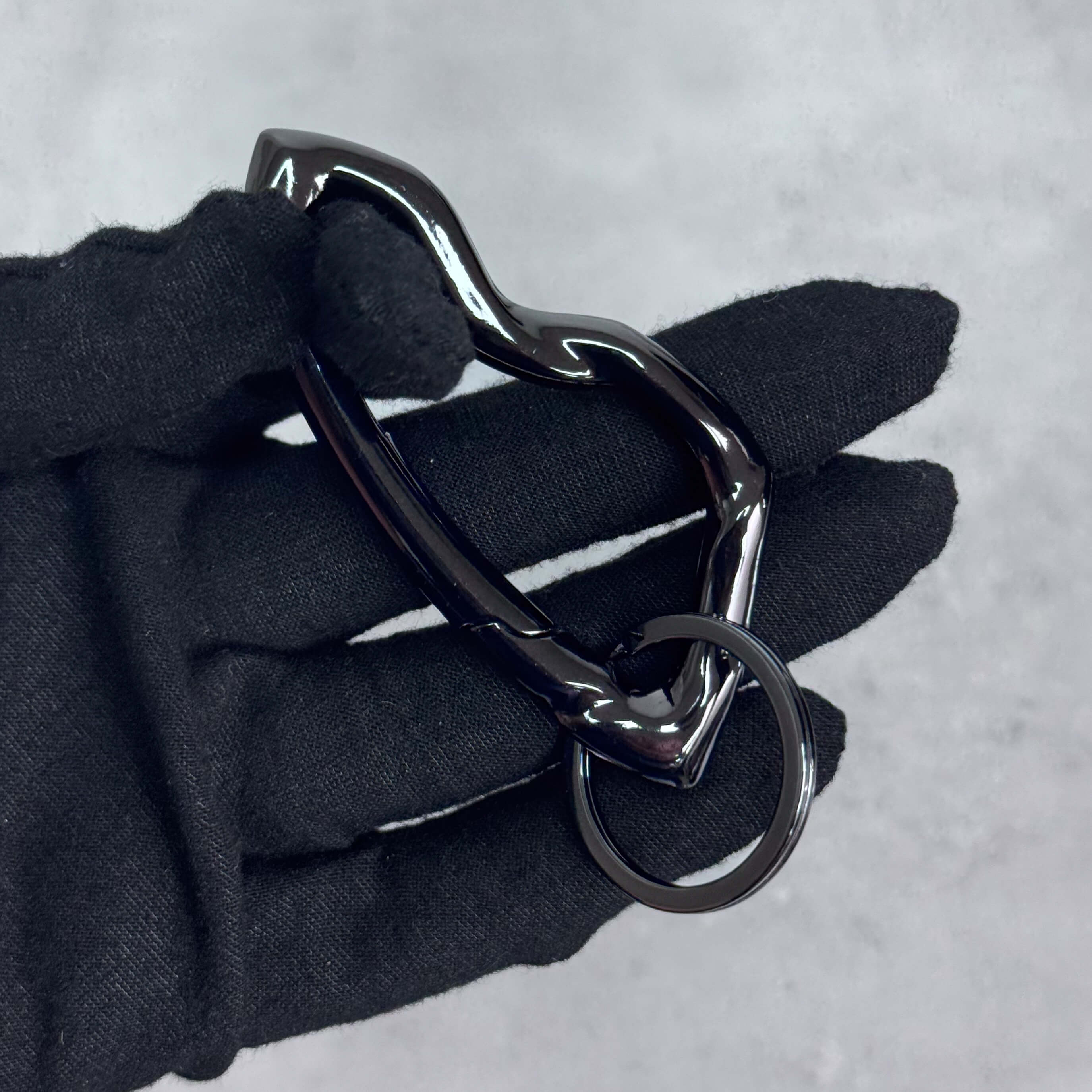 Glossy black Irregular Y2K carabiner keychain with curvy modern shape displayed in gloved hand.