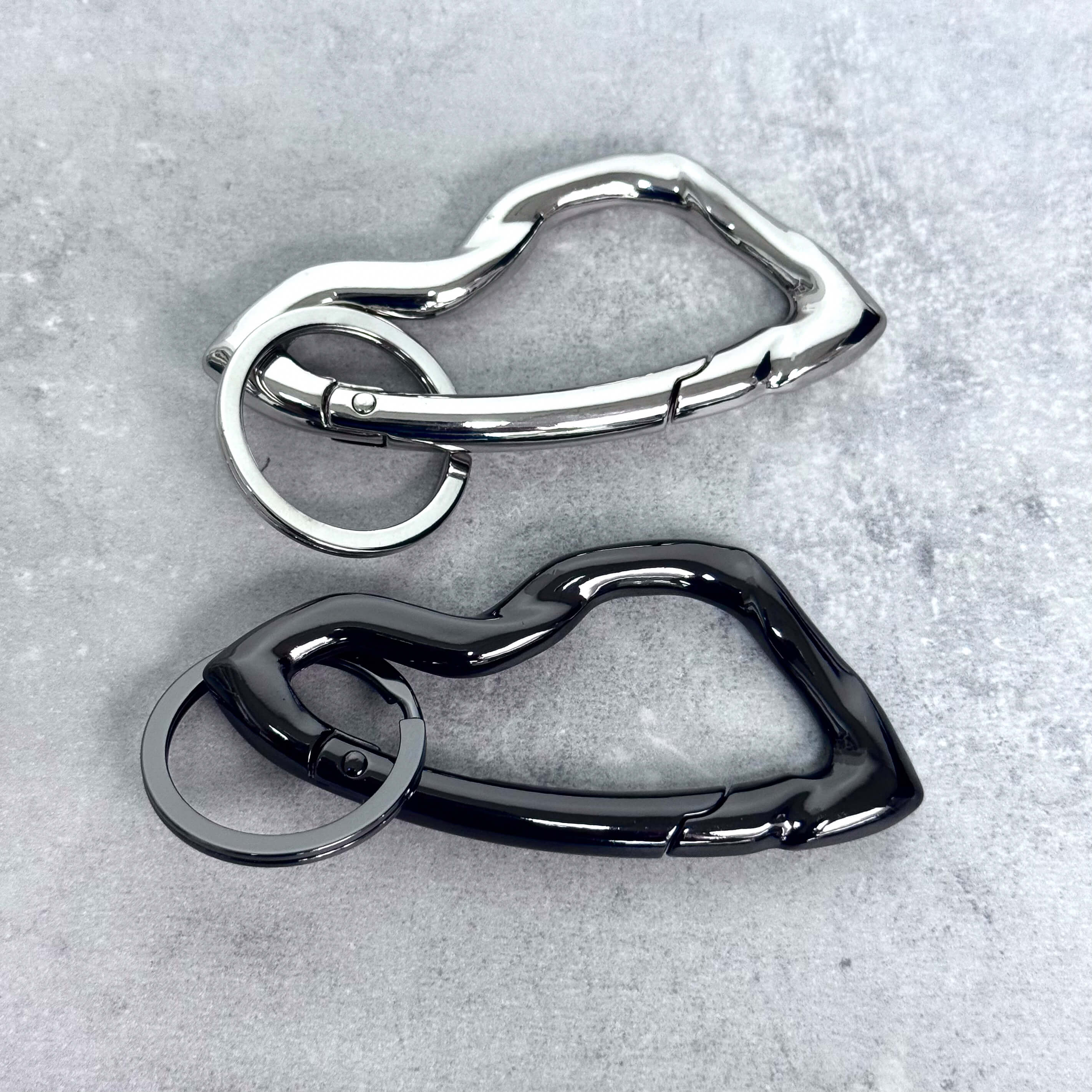 Silver and black Irregular Y2K carabiner keychains with sculpted wavy bodies displayed side by side.