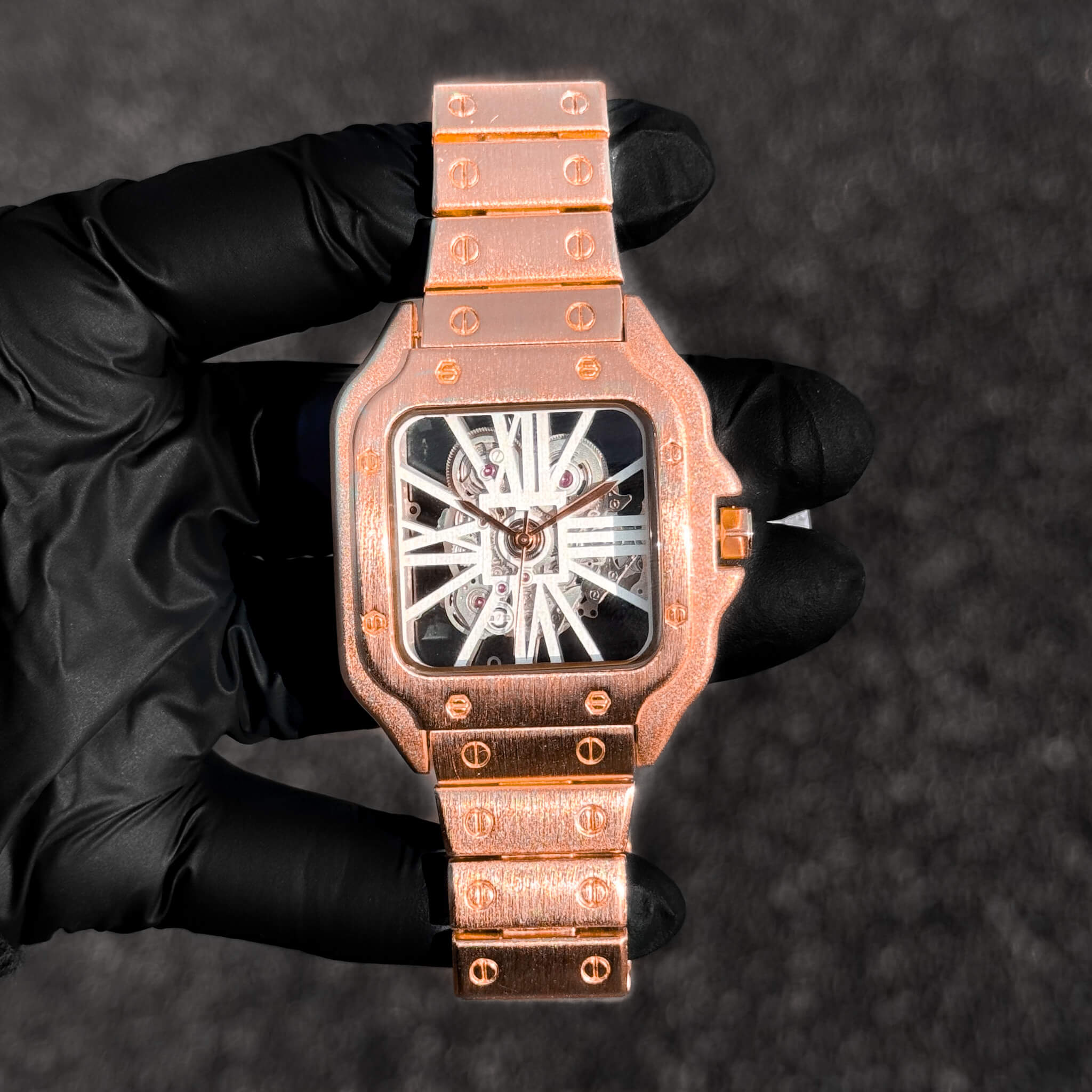 Men's 40mm rose gold square skeleton dial watch with brushed metal bracelet and visible mechanics.