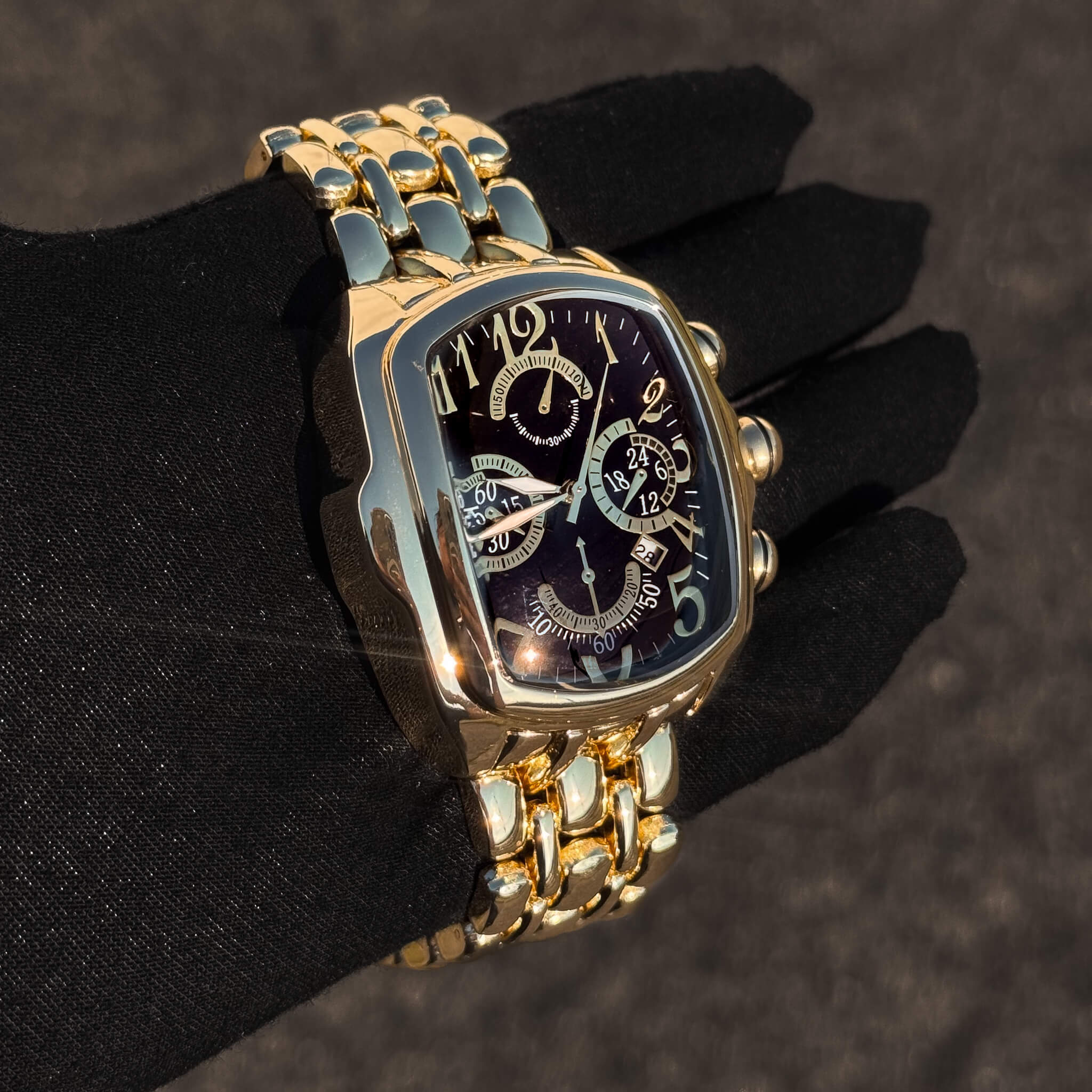 Men’s 43mm gold tonneau watch with black chronograph dial and high-shine linked bracelet.