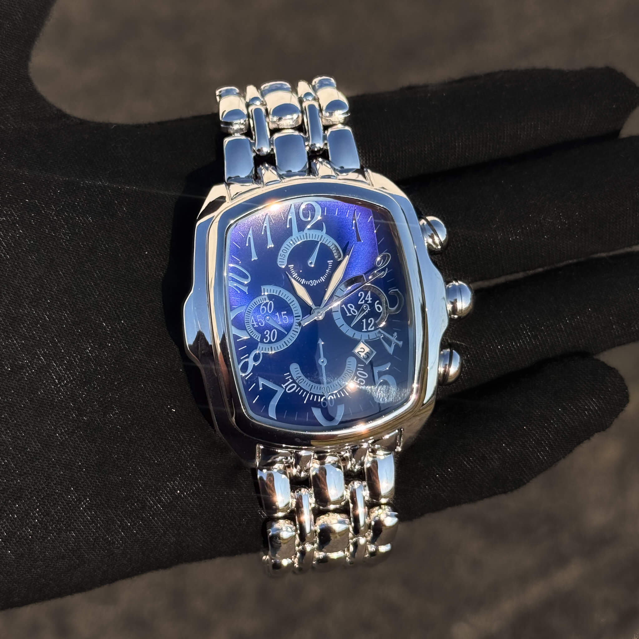 Men’s 43mm tonneau watch with blue chronograph dial and silver metal band, quartz movement.