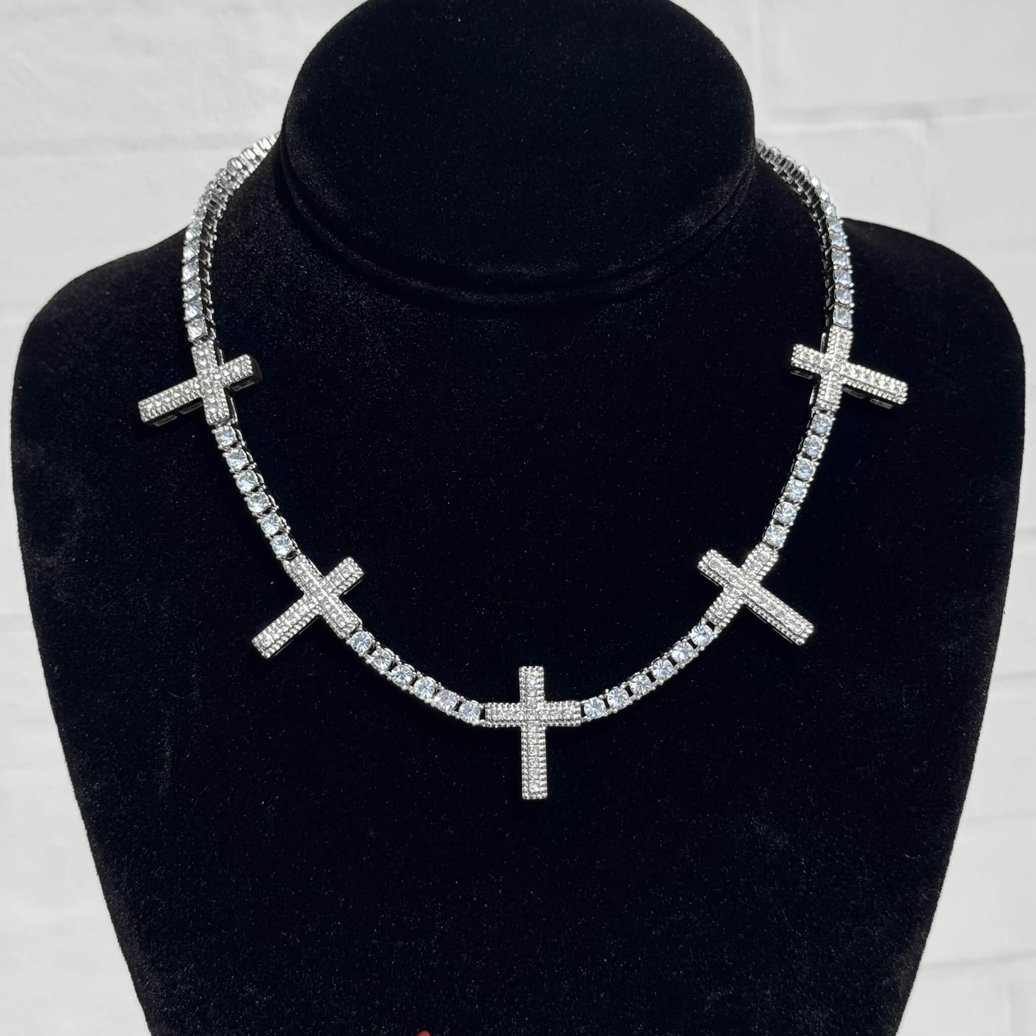 Silver Iced Cross Tennis Choker with shimmering pavé cross charms shown on a black velvet display stand.