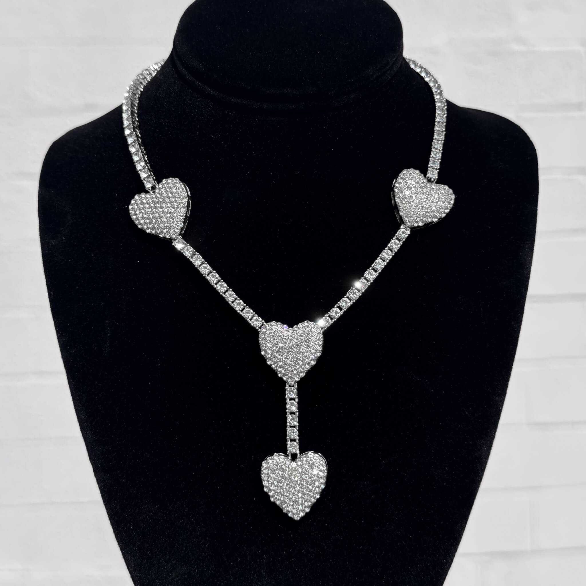 Silver Iced Heart Lariat Tennis Necklace with pavé crystal heart pendants on a black velvet stand.