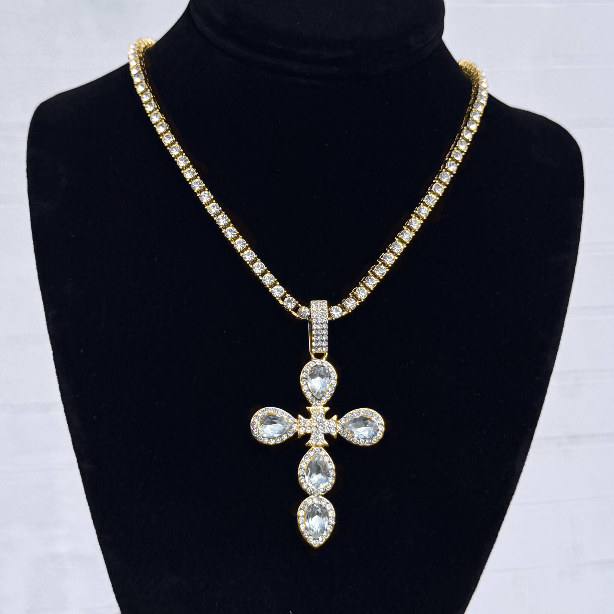 Iced Cross Tennis Necklace in gold with pear-cut crystal cross pendant displayed on black velvet stand.