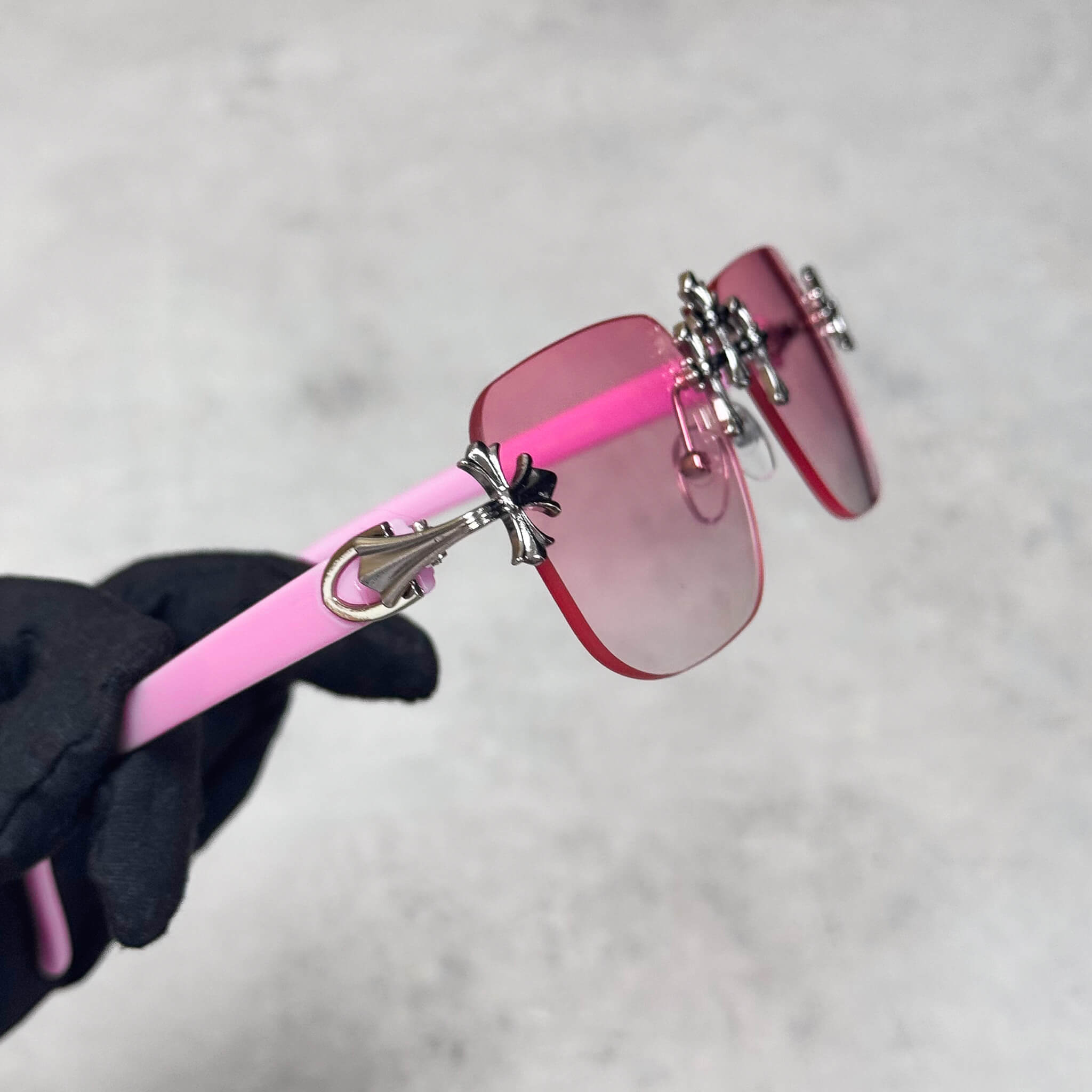 Side profile of pink Solid Triple Cross Sunglasses with silver cross temples and rimless lenses.