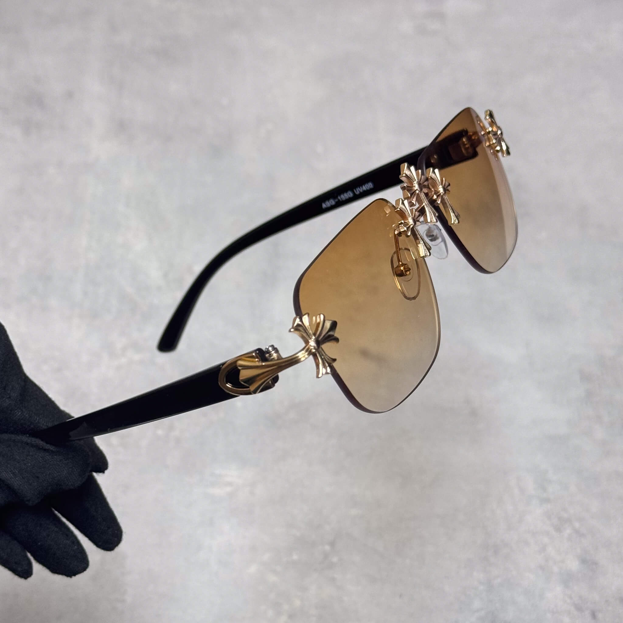 Gold Triple Cross sunglasses with brown lenses and black temples in angled side view.
