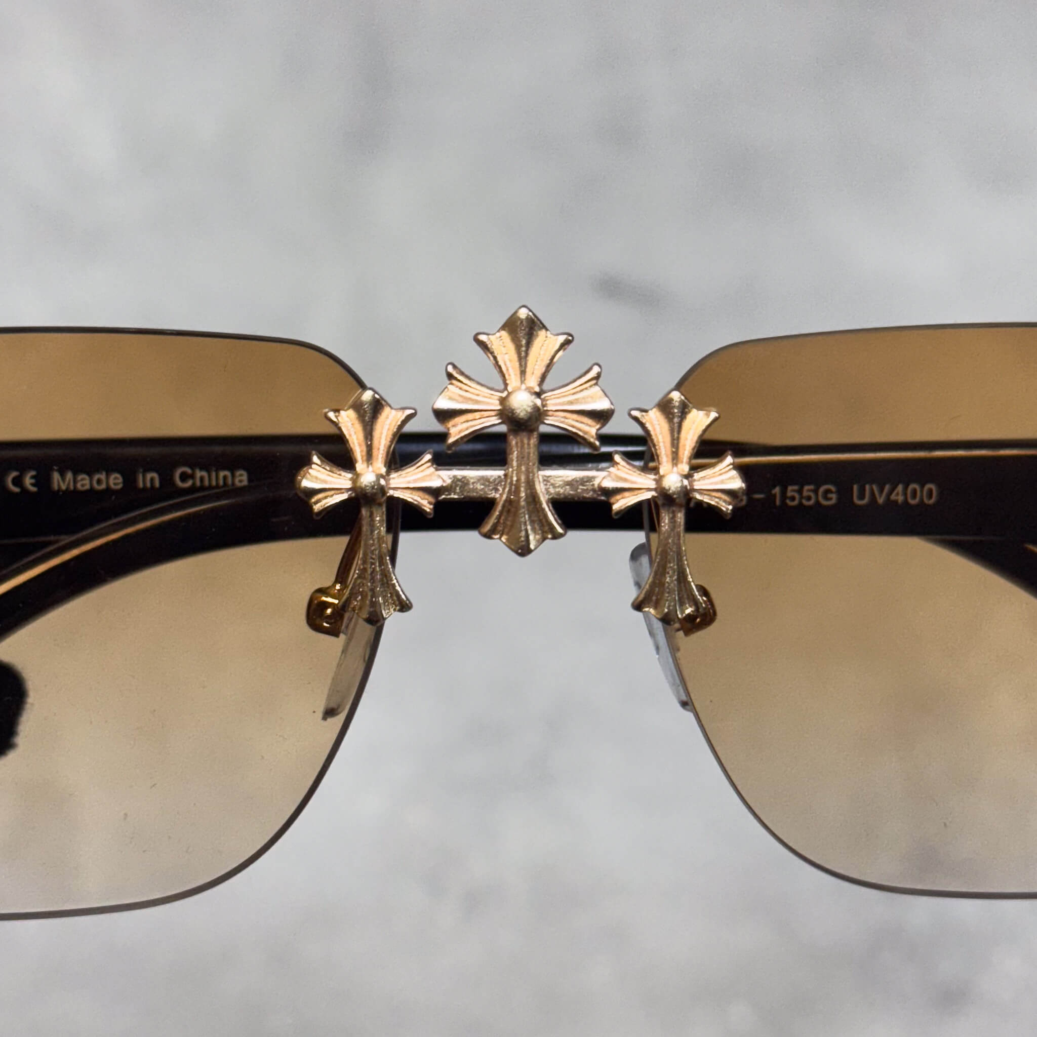 Close-up of gold Triple Cross detailing on brown lens luxury fashion sunglasses.