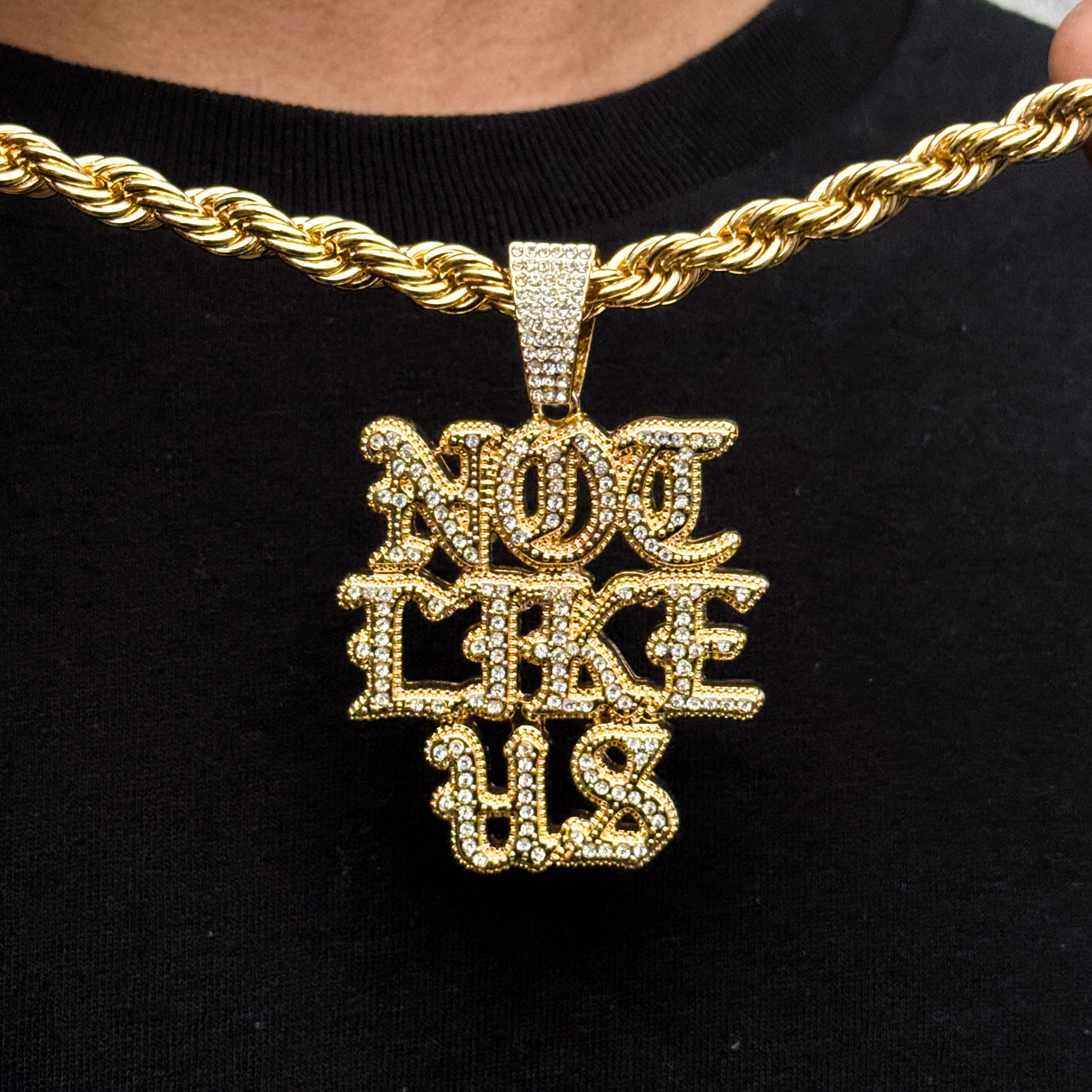 Gold iced out Not Like US pendant paired with an 8mm rope chain displayed close-up on chest.