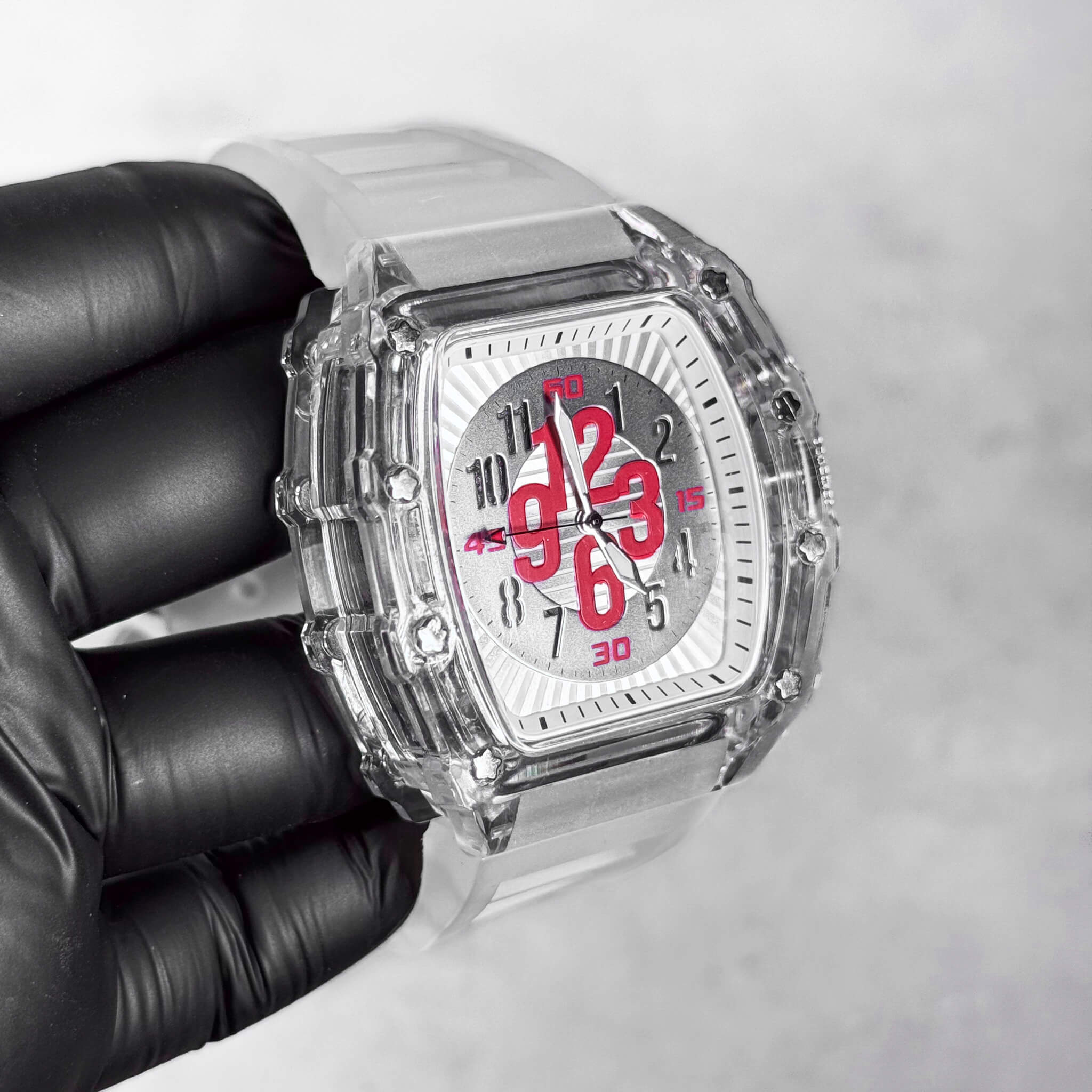 Men's 44mm Tonneau Dial Watch shown at an angle with clear case, white strap, and red dial numbers.