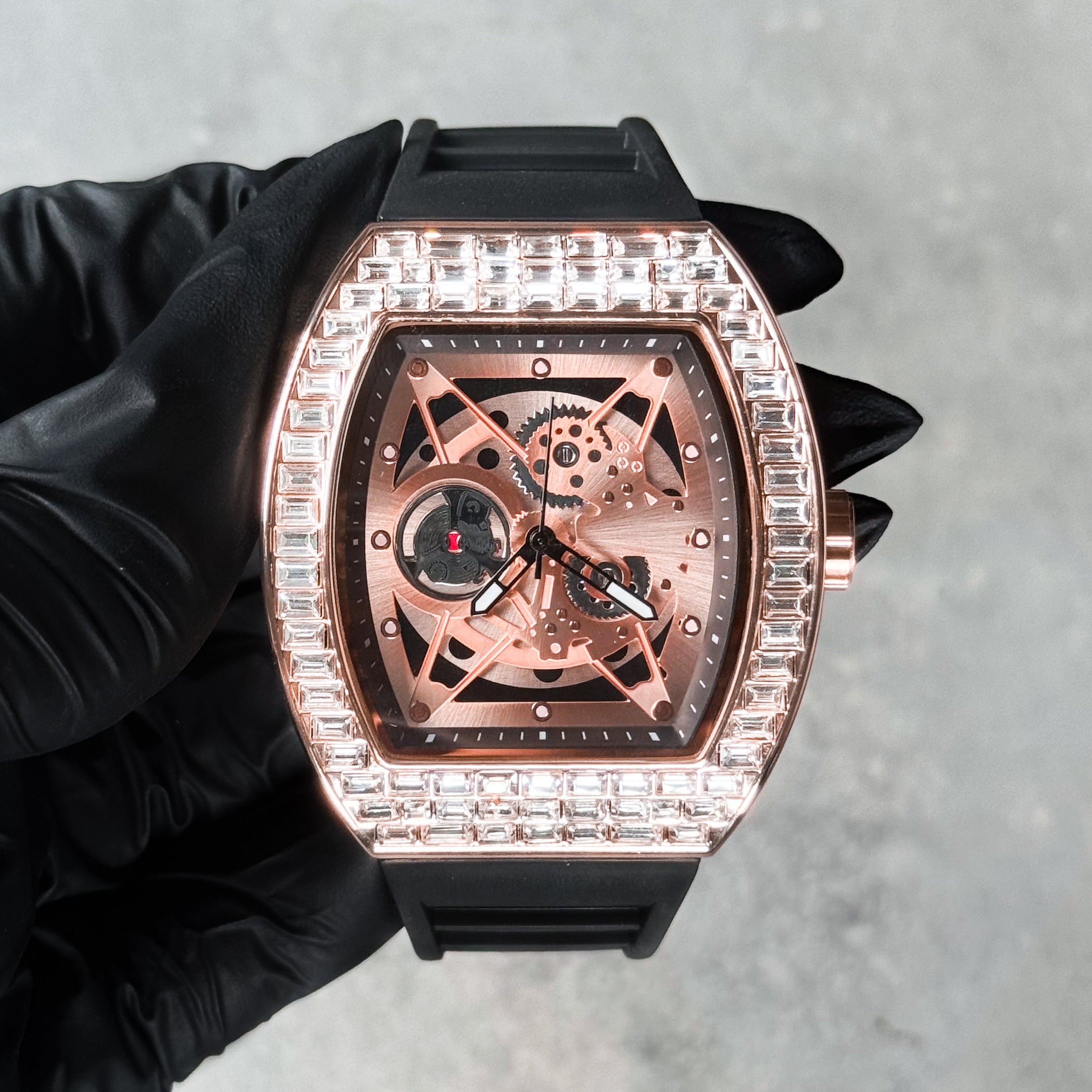 Rose gold men’s luxury iced watch featuring baguette crystal bezel, open-gear dial, and silicone strap.