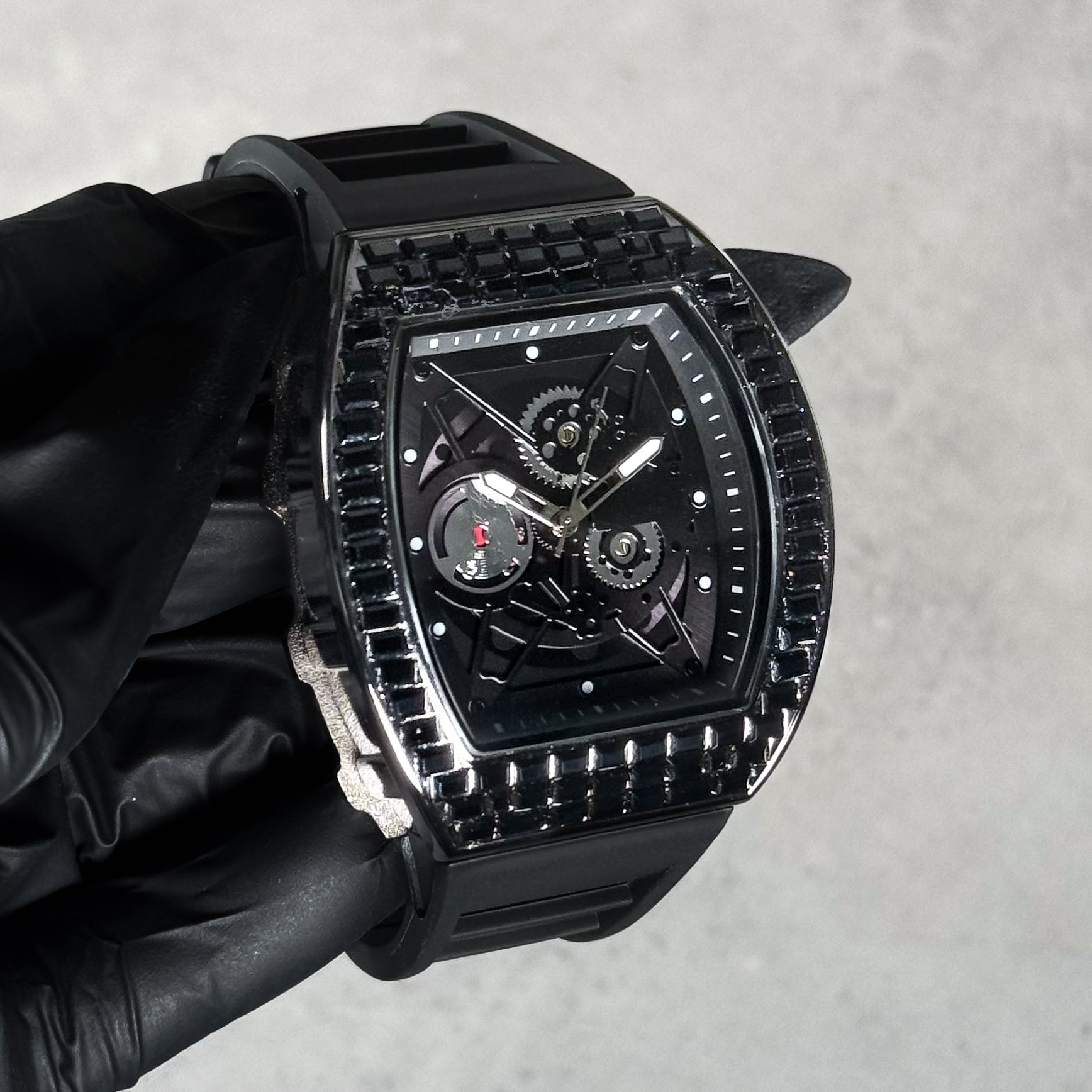 Black men’s luxury iced watch with dark baguette bezel, skeleton dial design, and silicone wrist band.