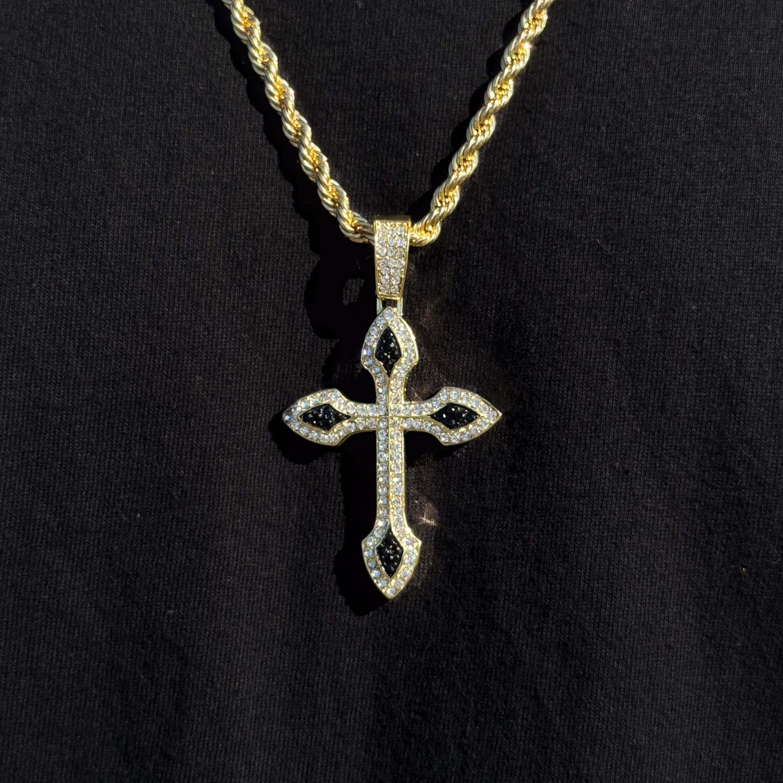 Gold large iced-out cross pendant with black stone accents, paired with a thick gold rope chain.
