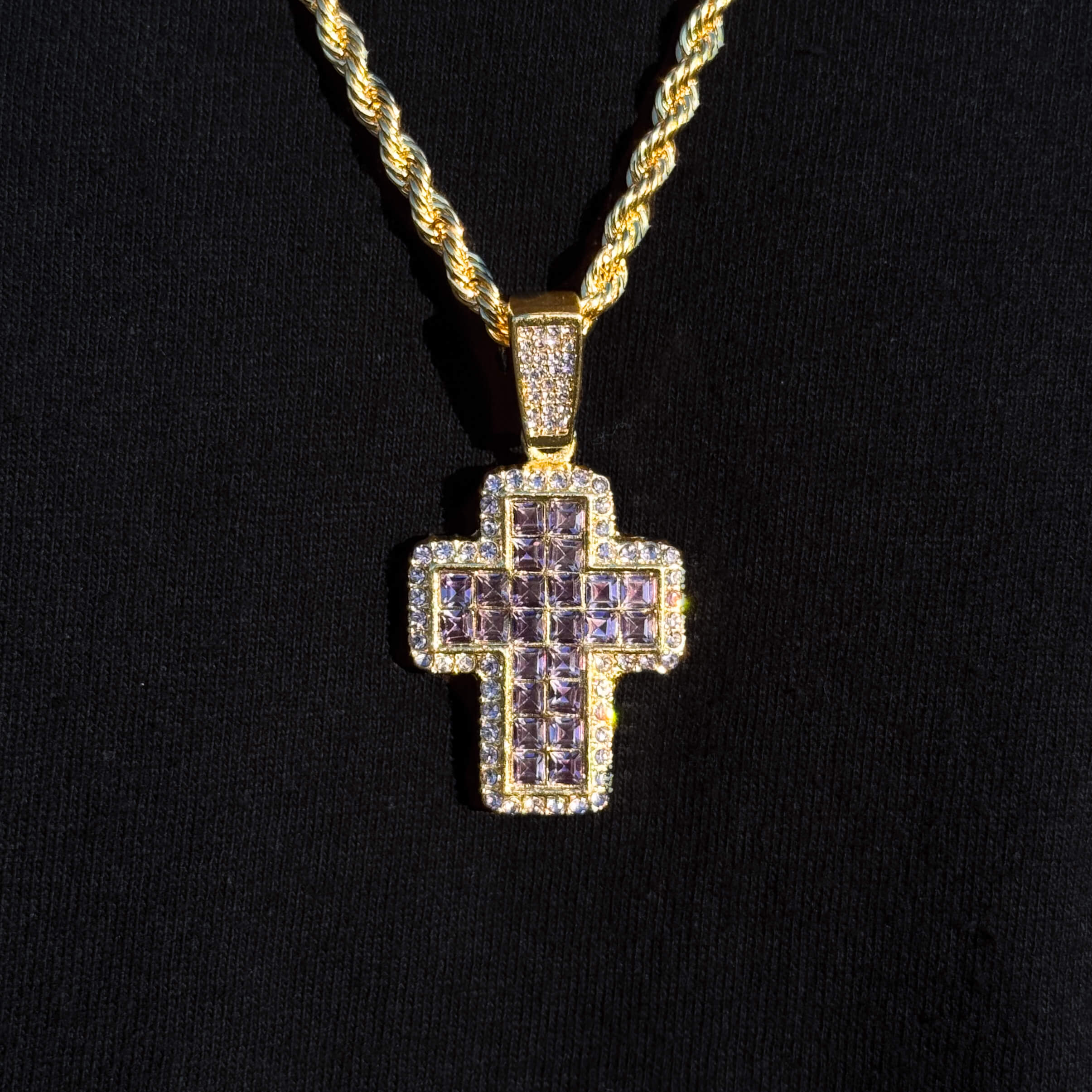 Gold medium purple cross pendant with halo stones on men's 5mm rope necklace in sunlight.
