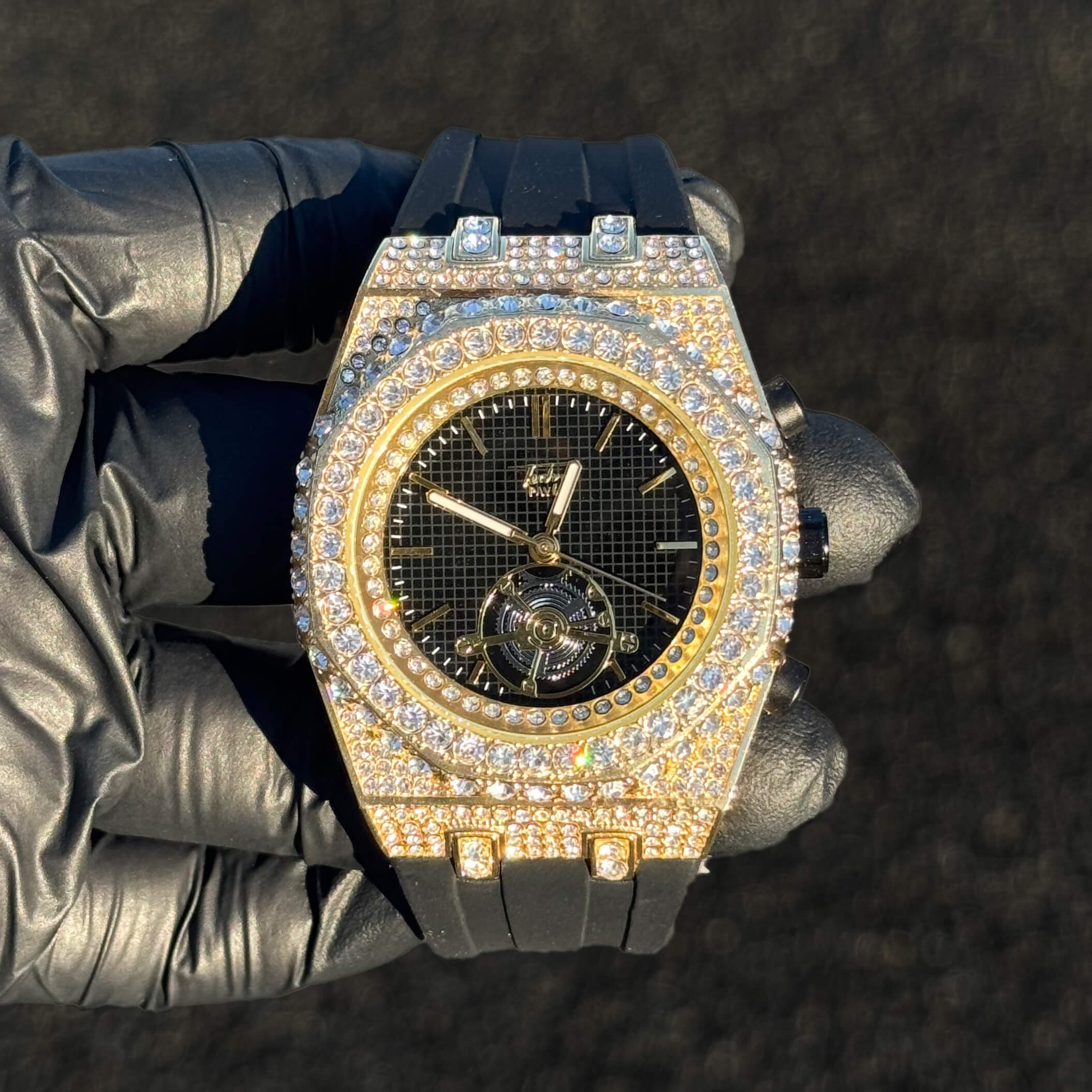 Men's 43mm iced out octagonal case watch with black dial, gold bezel, and black silicone band.