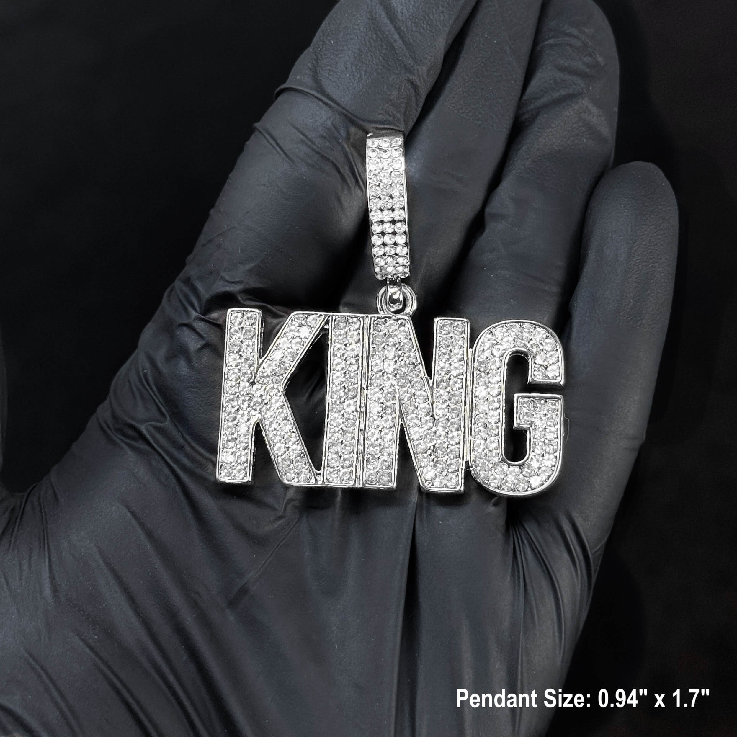Close-up silver iced-out KING pendant for men, large pavé letter design held in gloved hand.