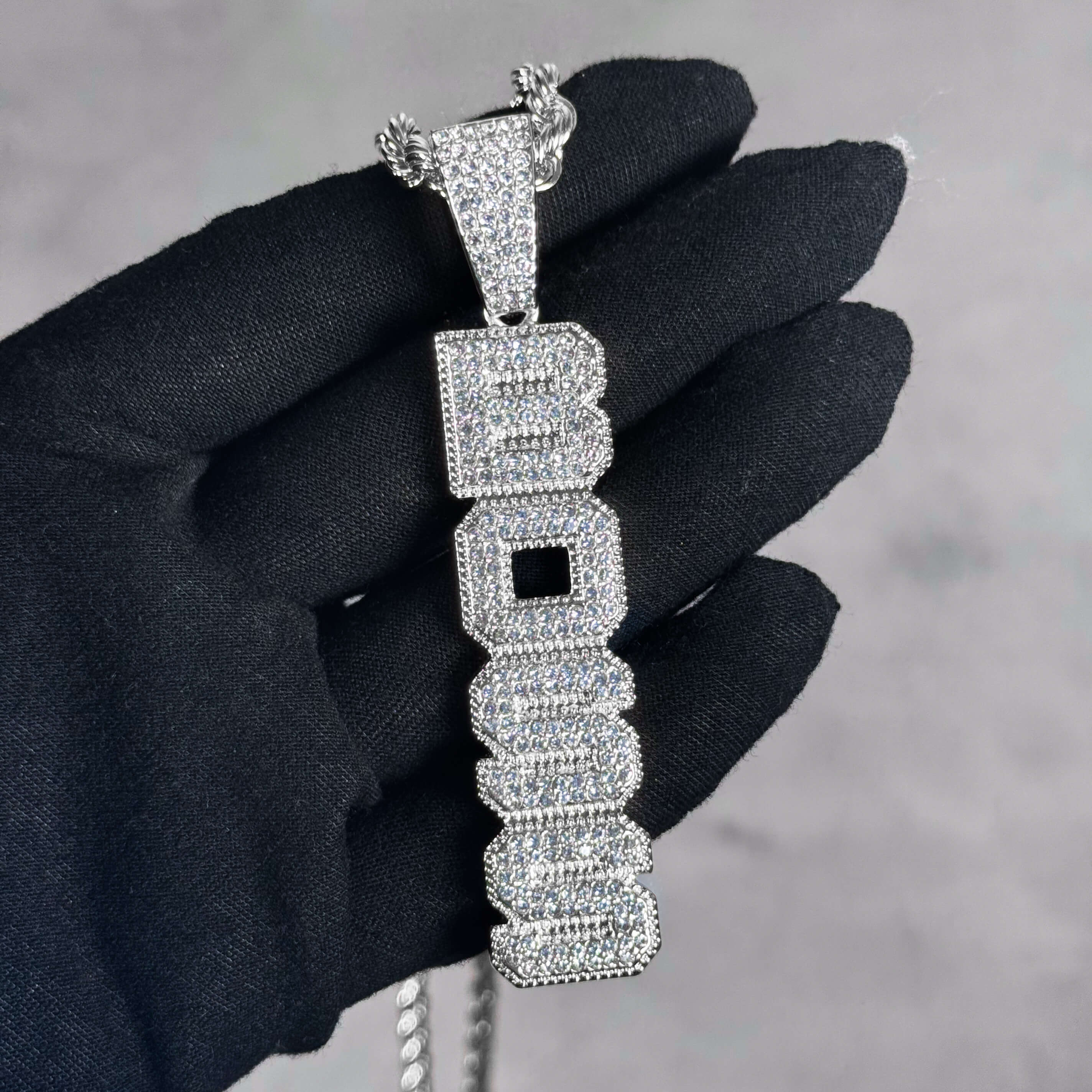 Silver Iced out Vertical Boss Pendant shown in hand, fully iced CZ letter design on rope chain.