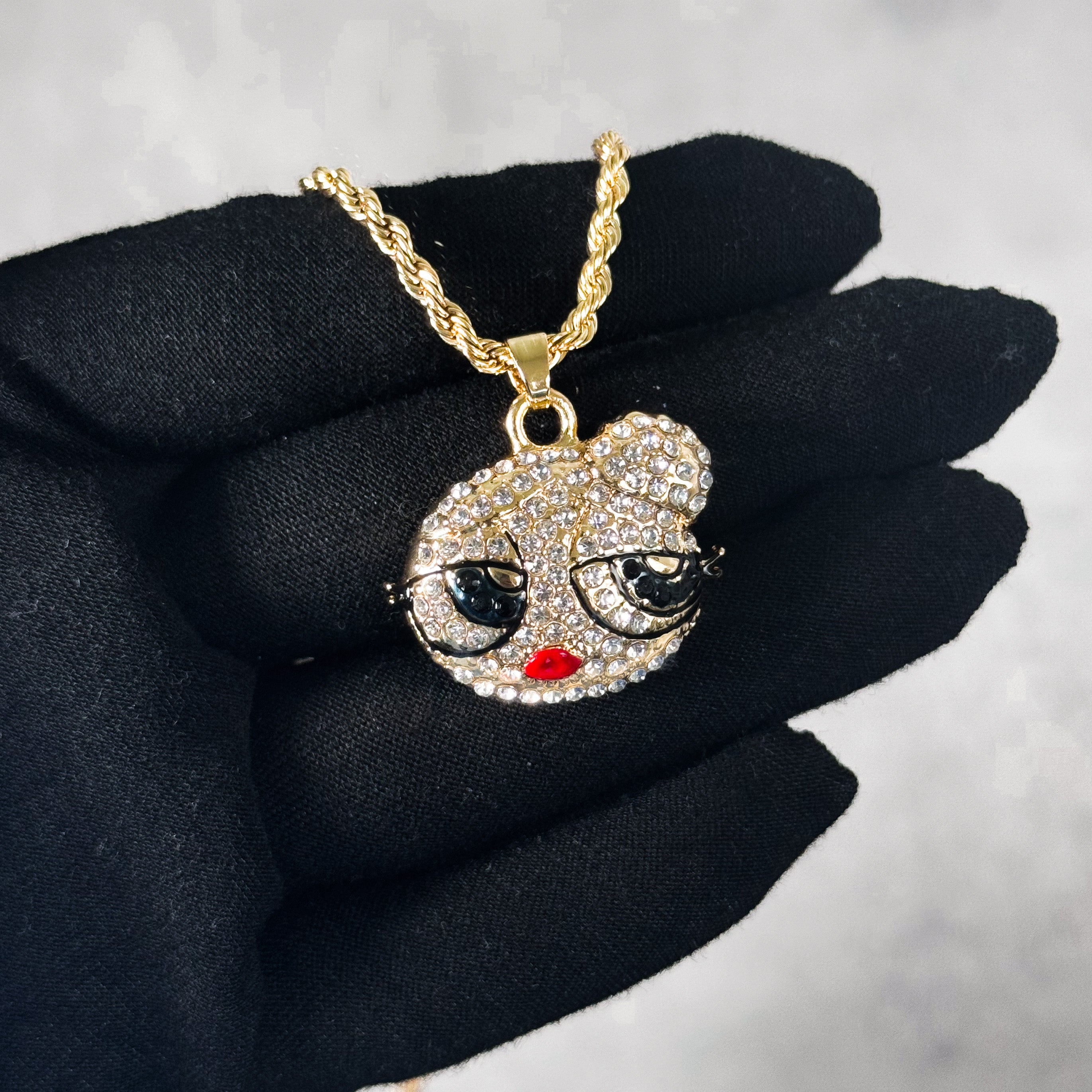 Mini Iced Out Hair Bun Doll Pendant in gold finish featuring crystal face detail, shown on hand.