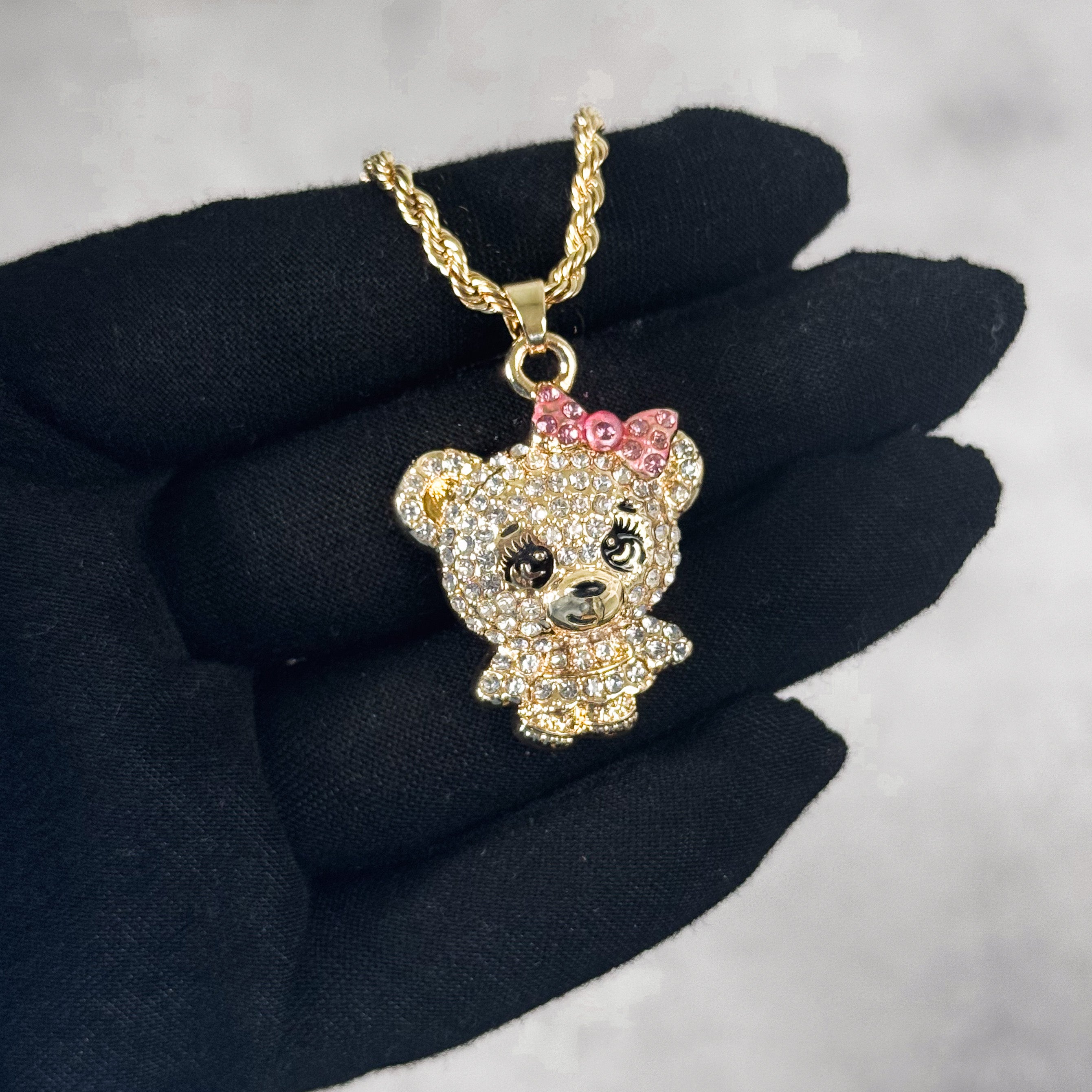 Hand-held gold Mini Iced Out Cute Bear Doll Pendant featuring pink bow and sparkling stones.
