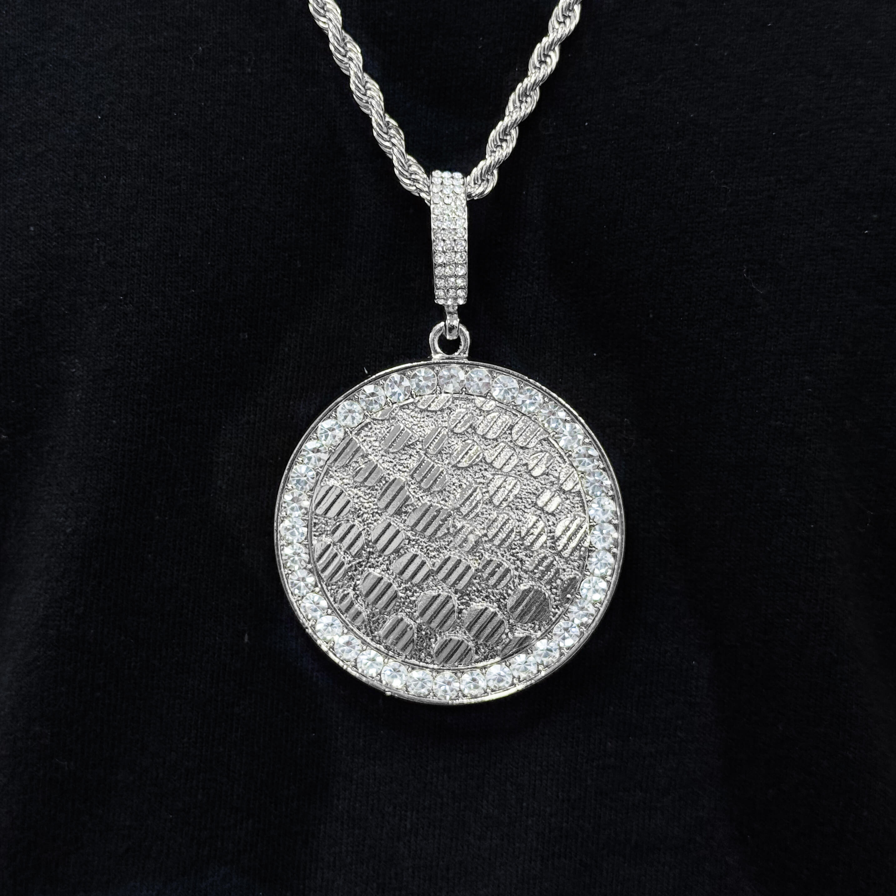 Men's silver iced-out medallion pendant with crystal border and textured center on chain.