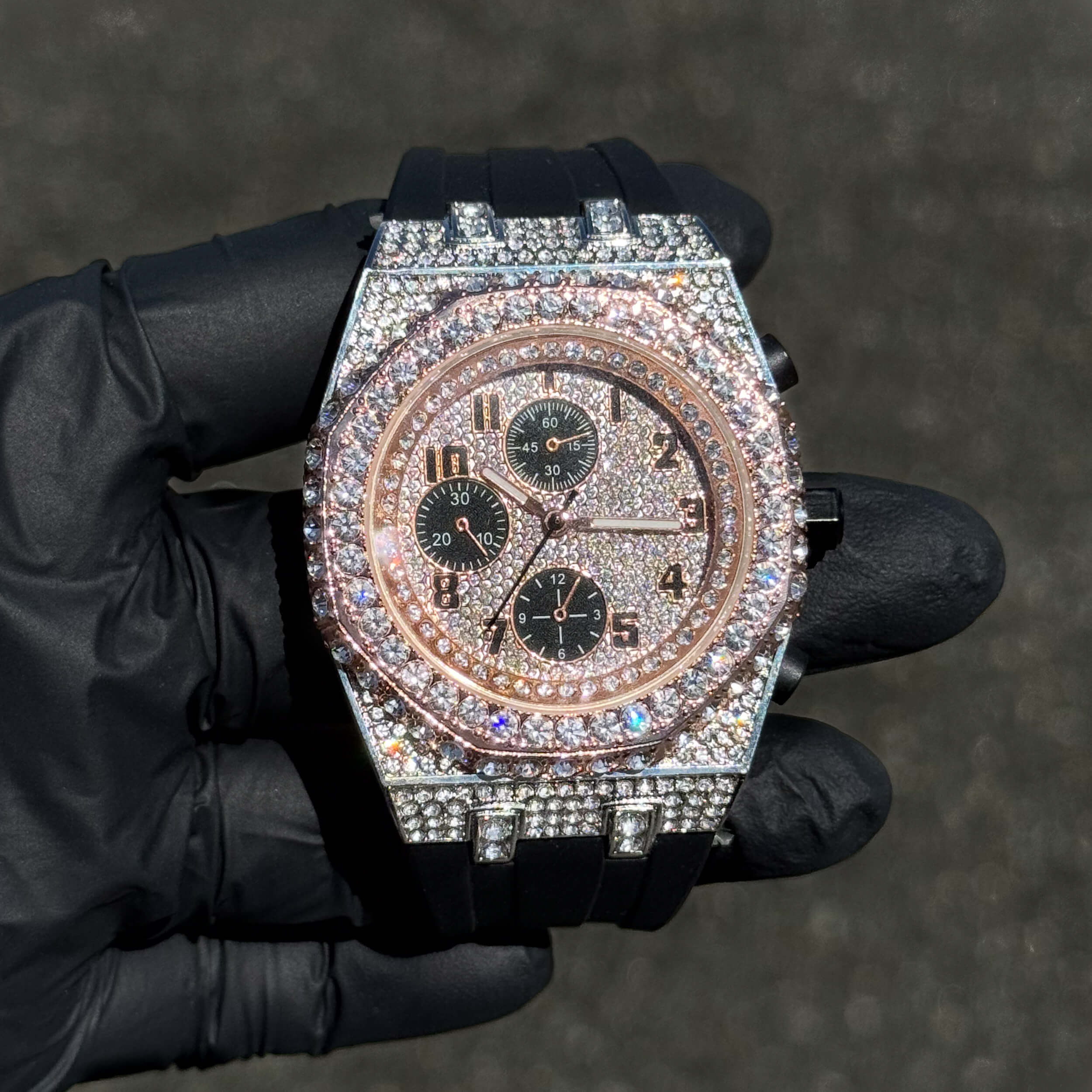 Men's 43mm rose gold iced out octagon bezel diamond watch with black silicone band and chronograph dial.