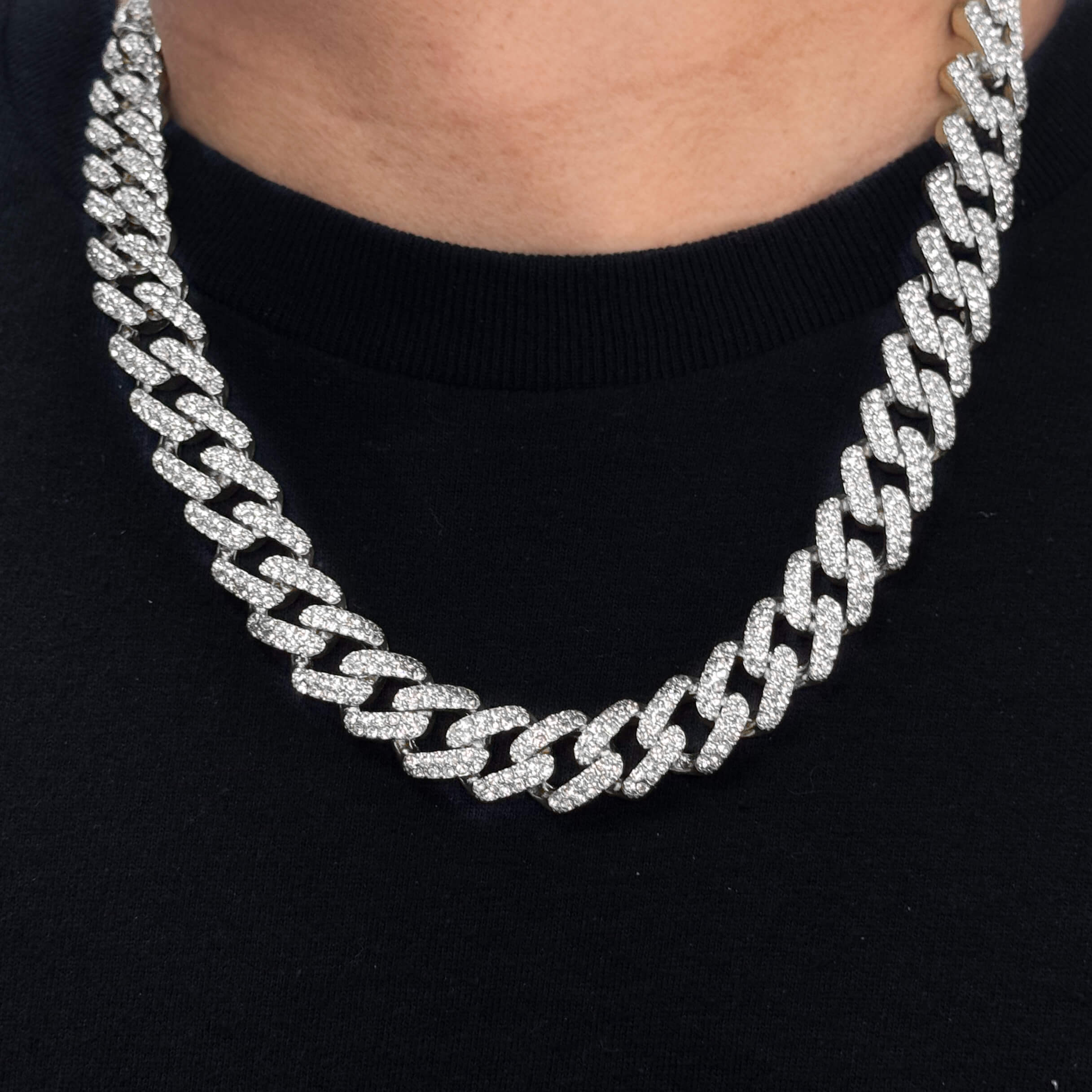 12mm Iced Out Cuban Chain in silver with pavé CZ stones, worn close-up around neck against black shirt.