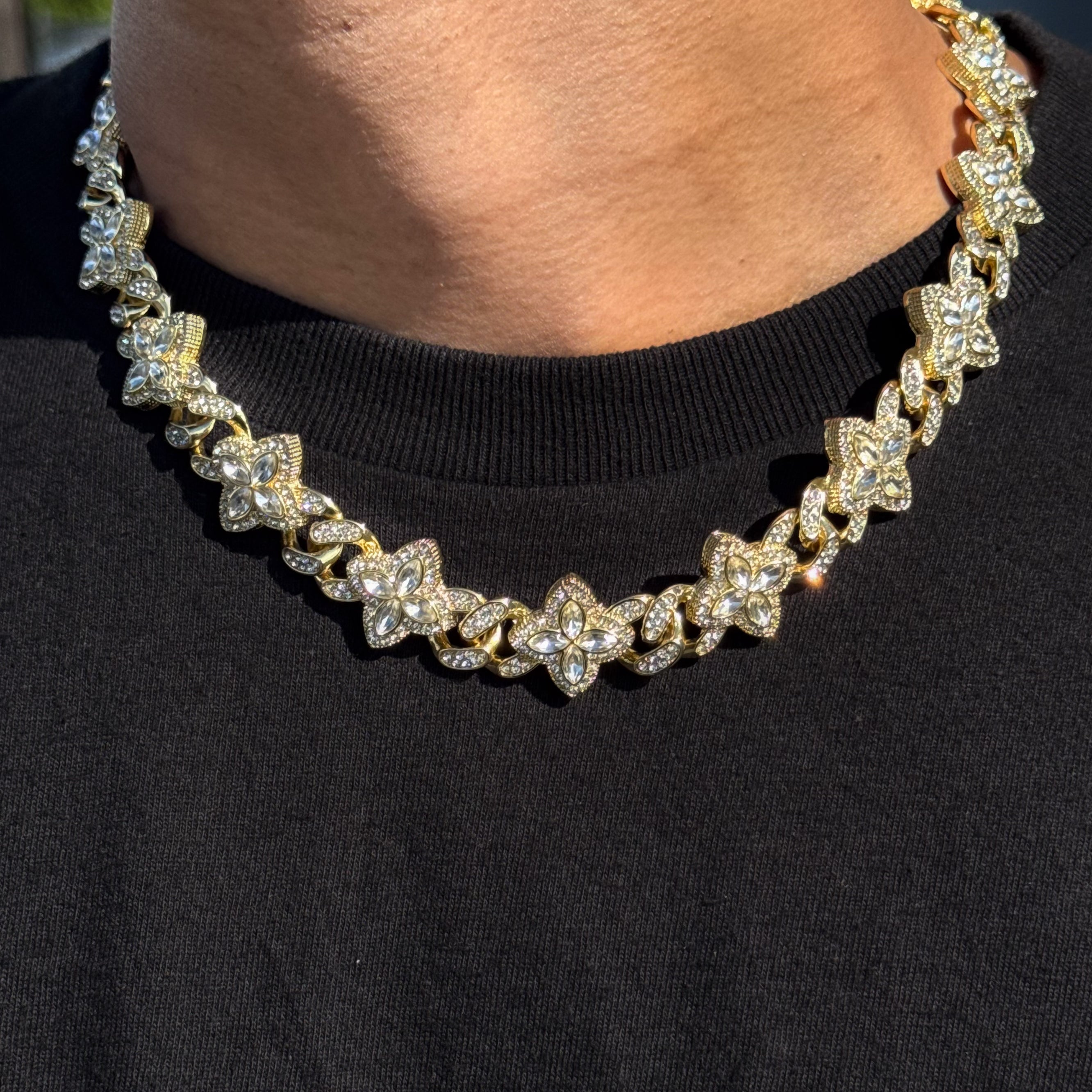 Gold Iced Clover Cuban Chain with clear stones, featuring shimmering pavé clover links worn over black shirt.