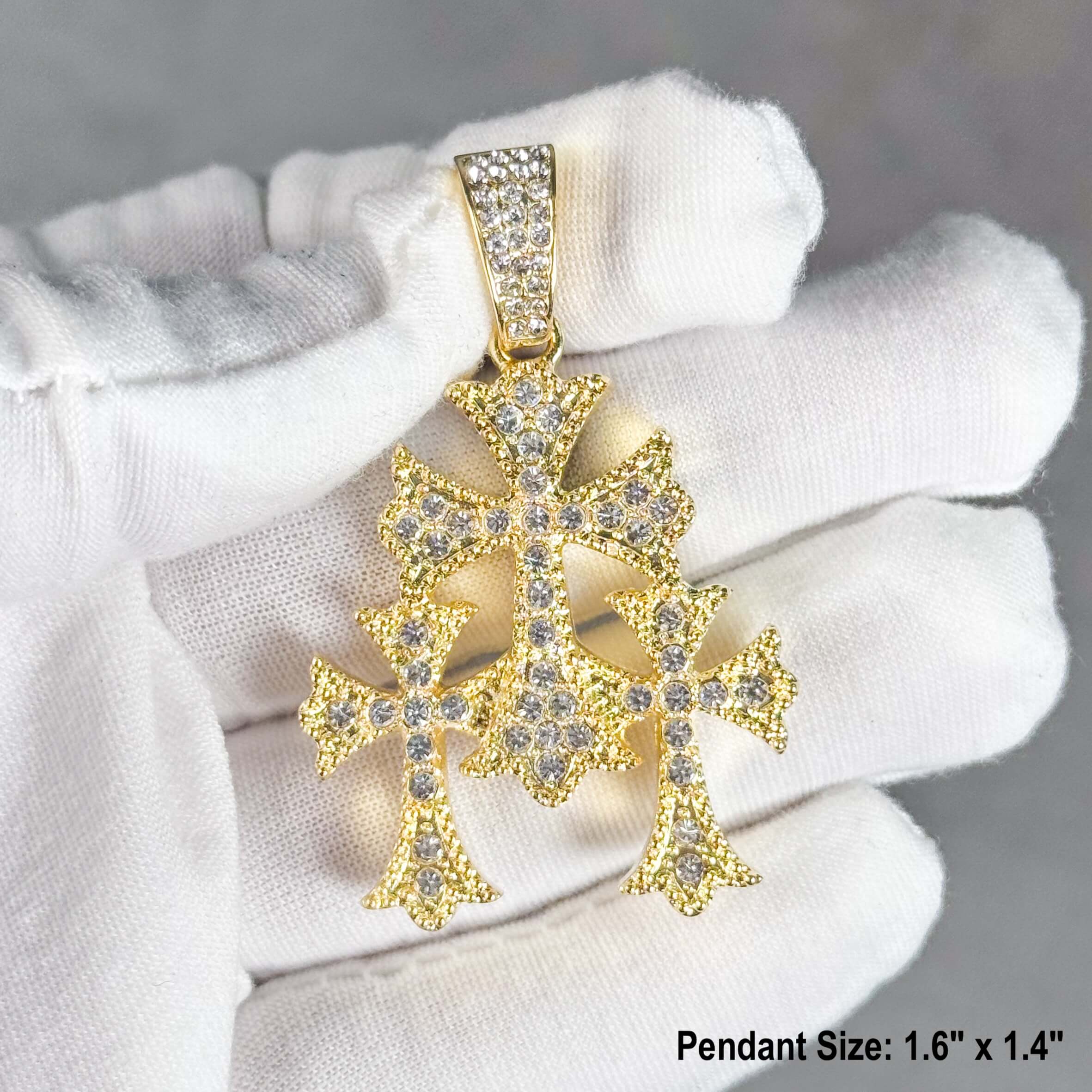 Gold men’s triple cross pendant iced out with clear stones, shown in hand for detail.