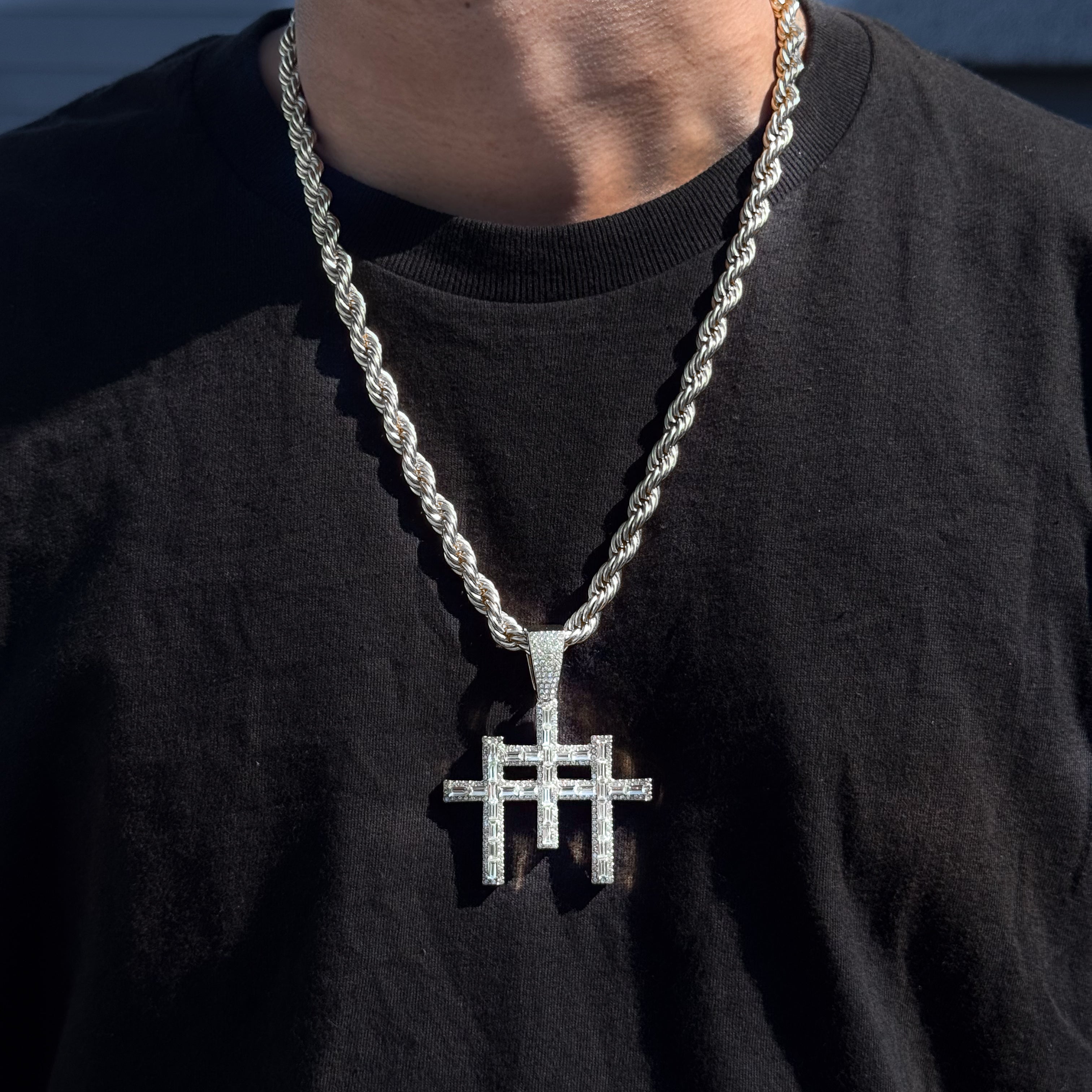 Men’s silver 55mm baguette iced-out cross pendant with 8mm rope chain worn outdoors.