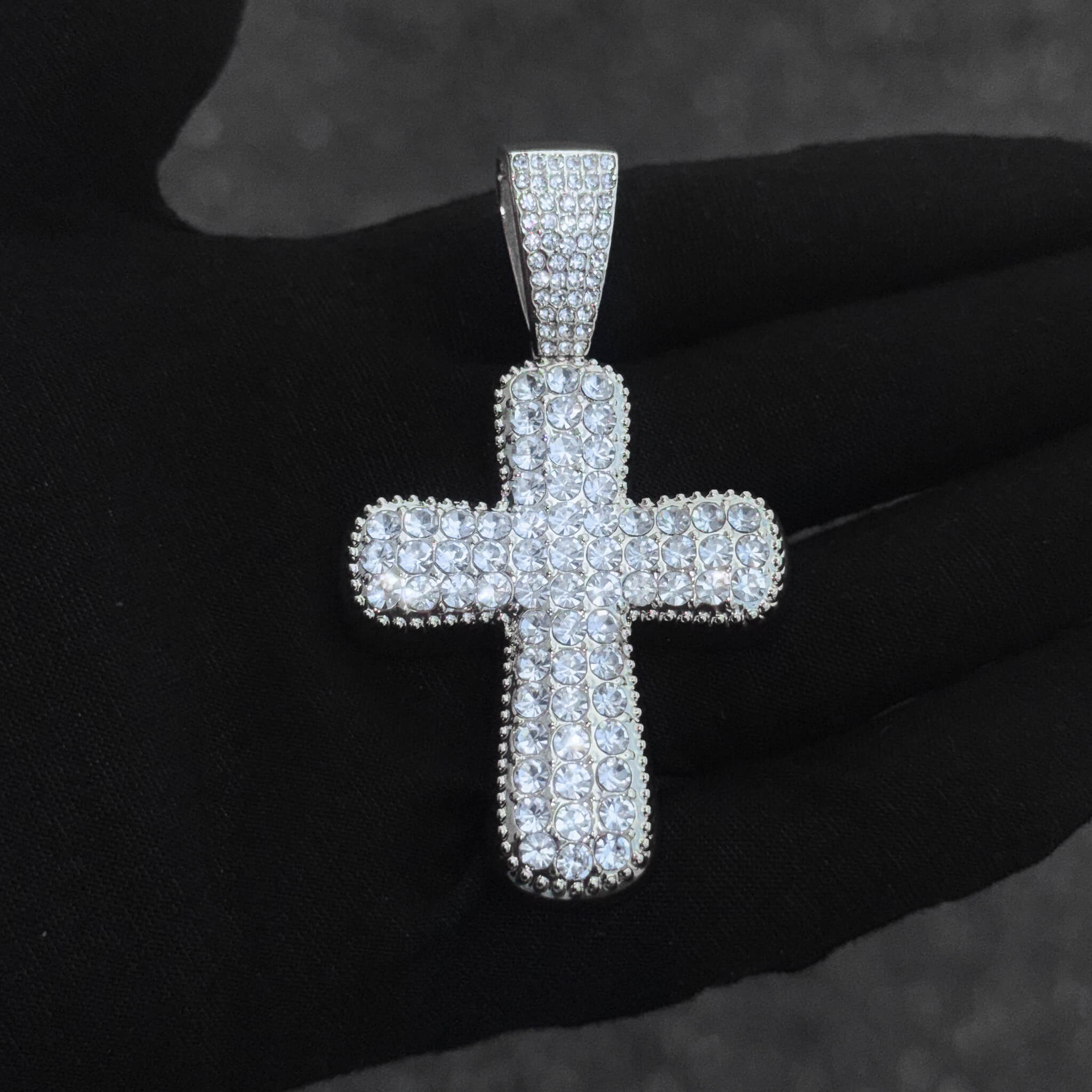 Detailed close-up of silver iced-out cross pendant featuring pavé crystal stones and polished shine.