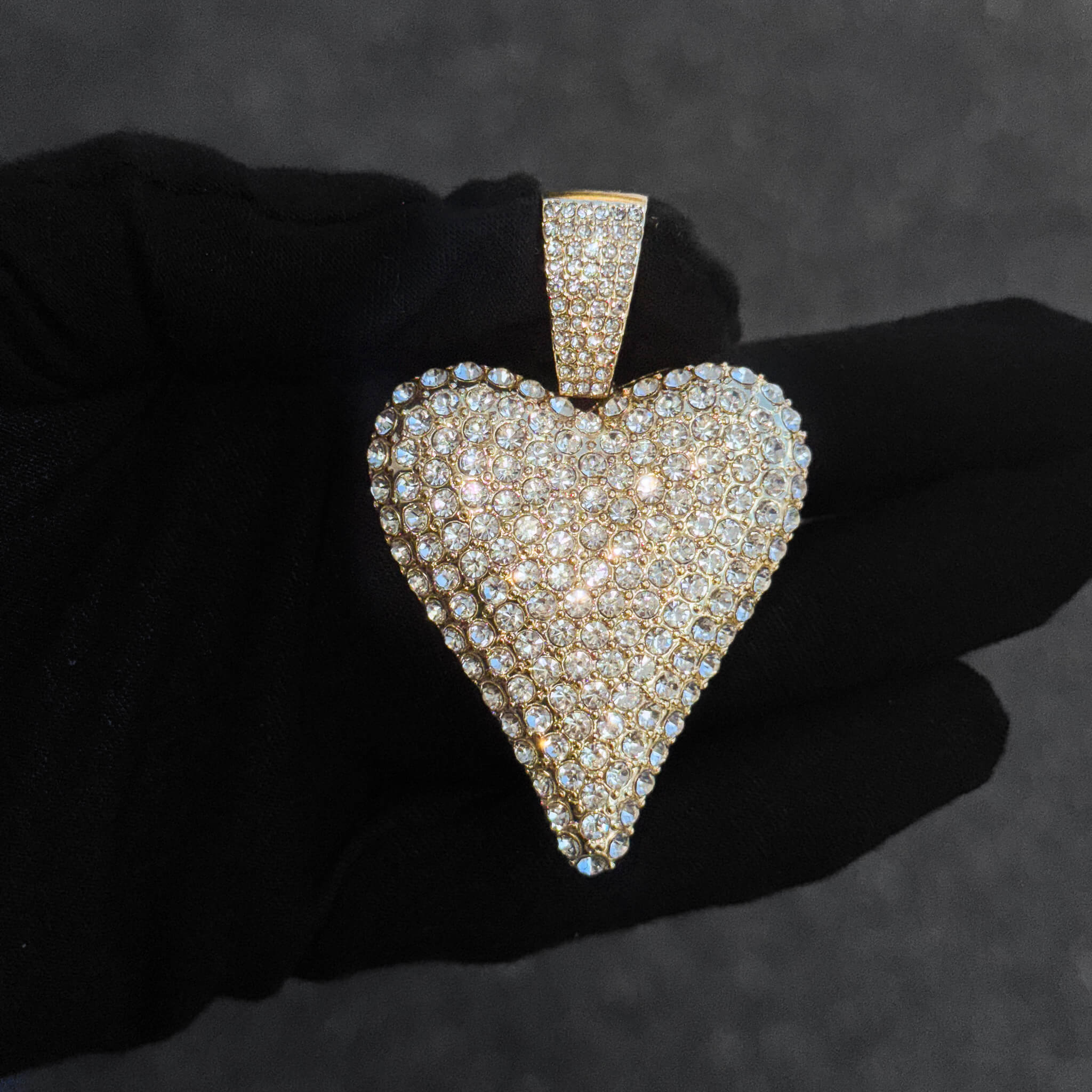 Close-up of gold iced-out 40mm heart pendant covered in round-cut crystals for women’s jewelry.