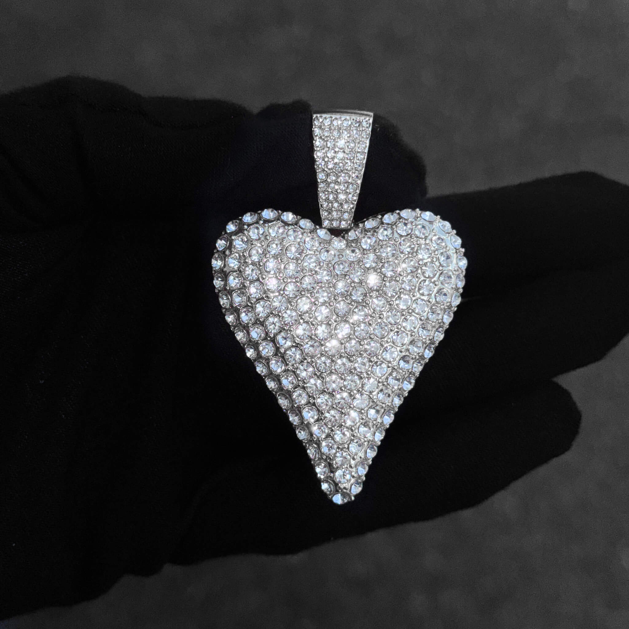 Detailed close-up of silver iced-out heart pendant featuring pavé stones and glossy shine.