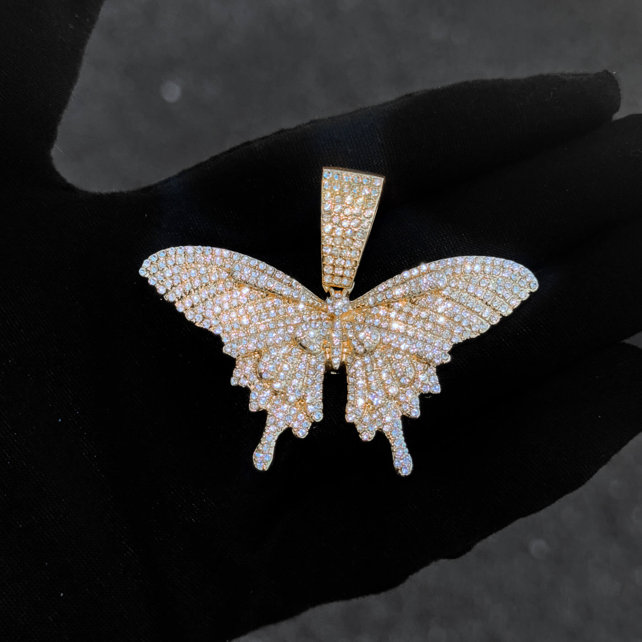 Close-up of gold iced-out 60mm butterfly pendant covered in sparkling stones for women’s jewelry.