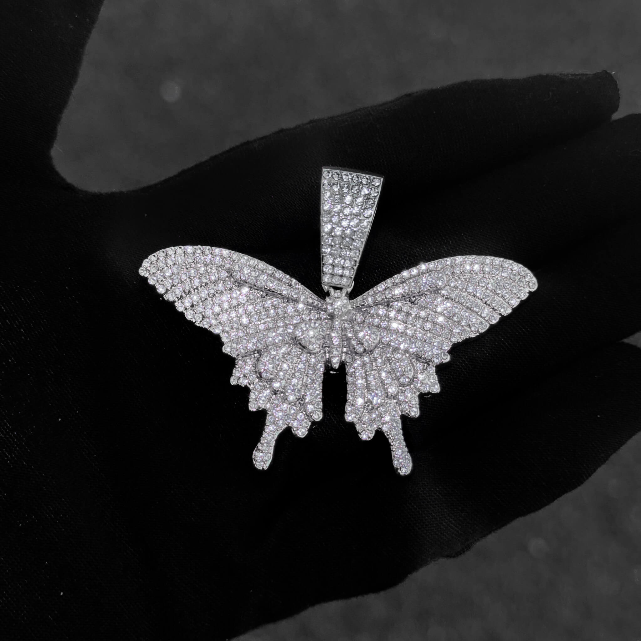 Detailed close-up of silver iced-out butterfly pendant showcasing crystal-paved wings and shine.