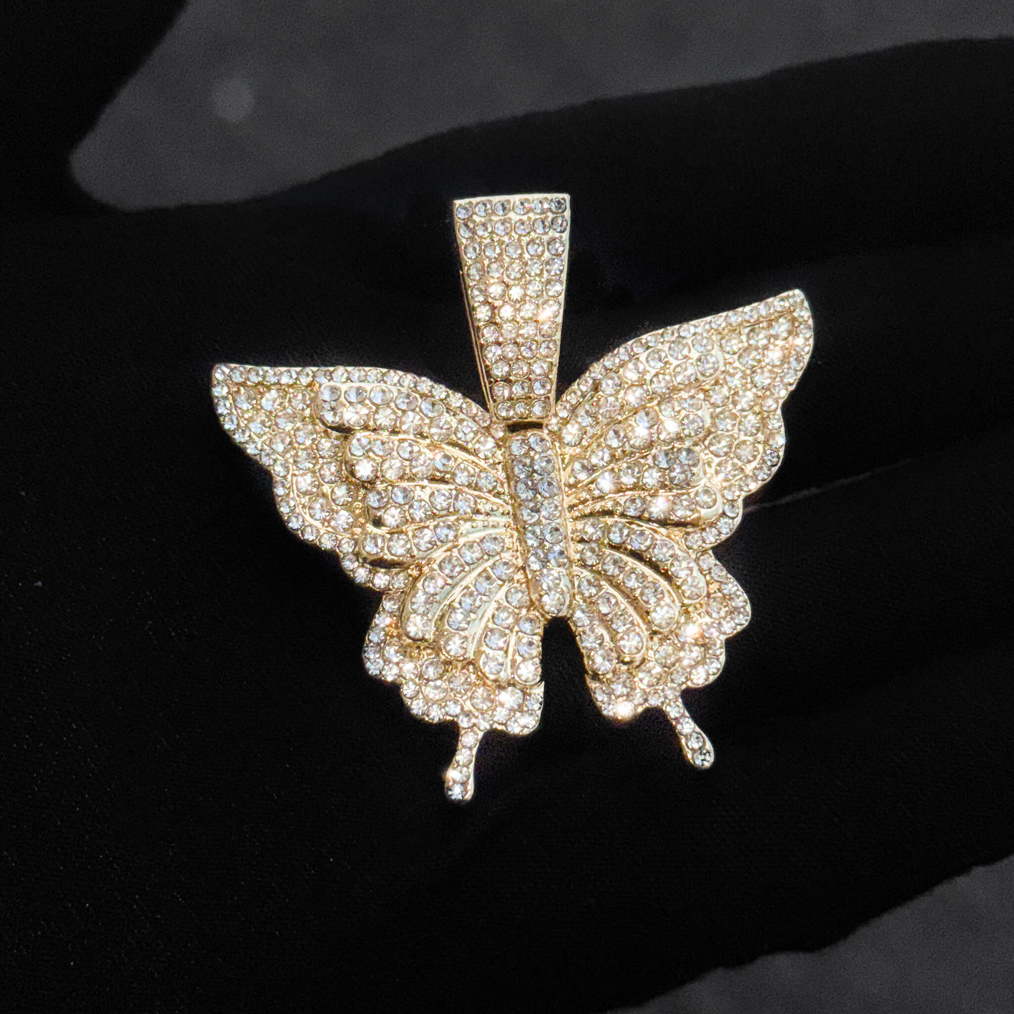 Close-up of gold iced-out butterfly pendant adorned with round-cut crystals for women’s jewelry.