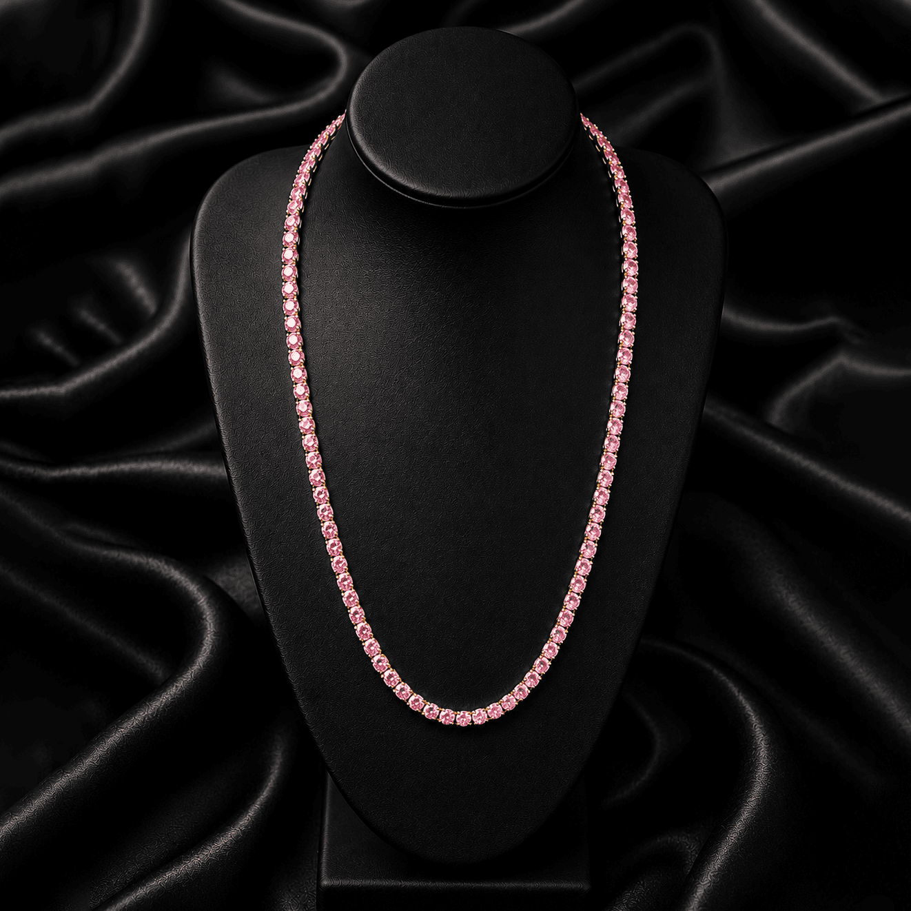 Pink moissanite tennis chain necklace displayed on a matte black jewelry bust against a black satin fabric background, showcasing a continuous row of round pink stones in a sleek, elegant design.