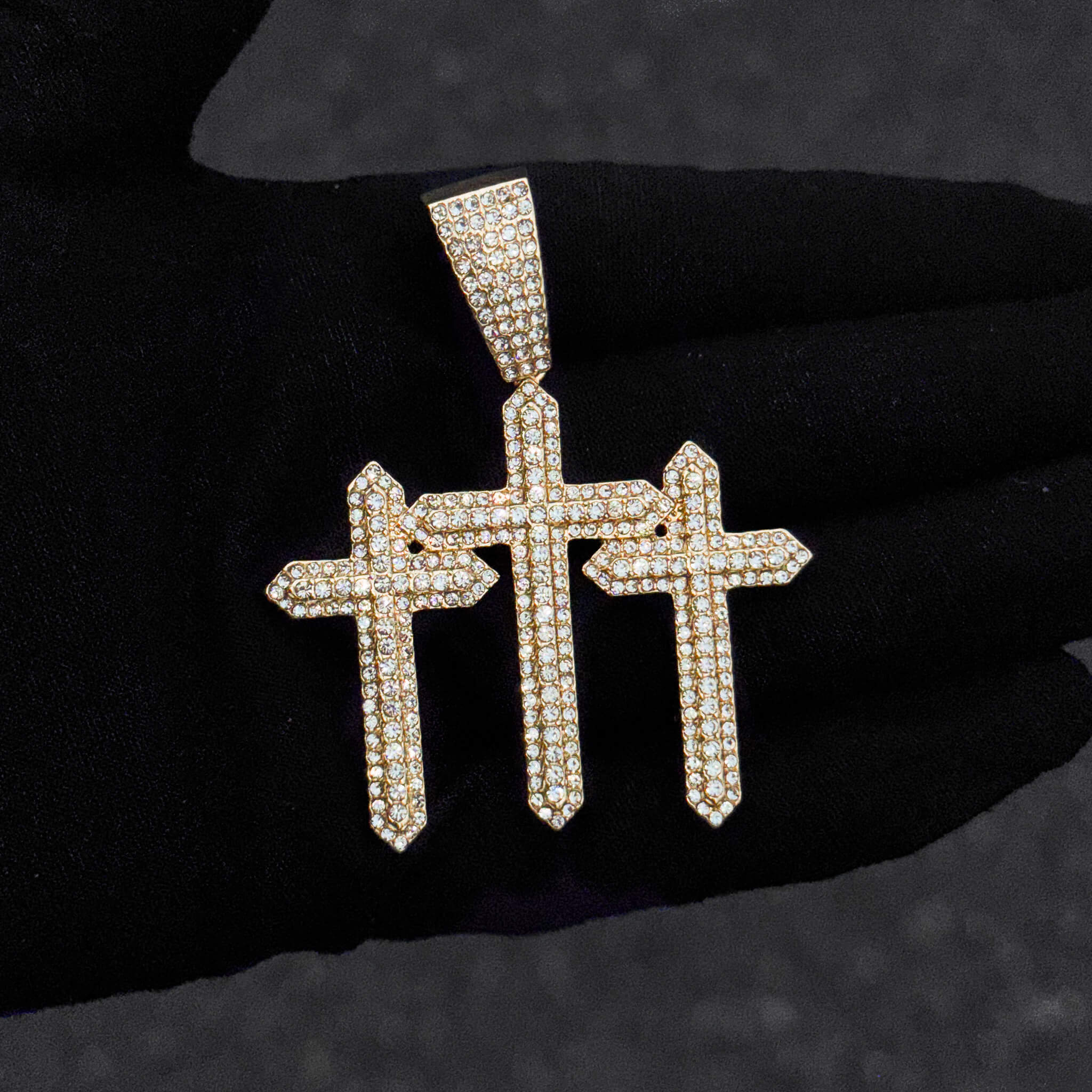 Close-up of gold 53mm iced-out triple cross pendant featuring dense round crystal detailing.
