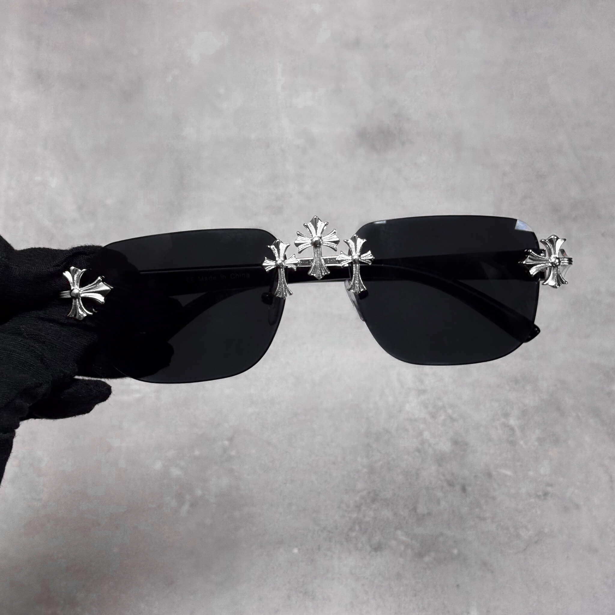 Rimless black lens sunglasses featuring silver Triple Cross detailing and slim black temples.