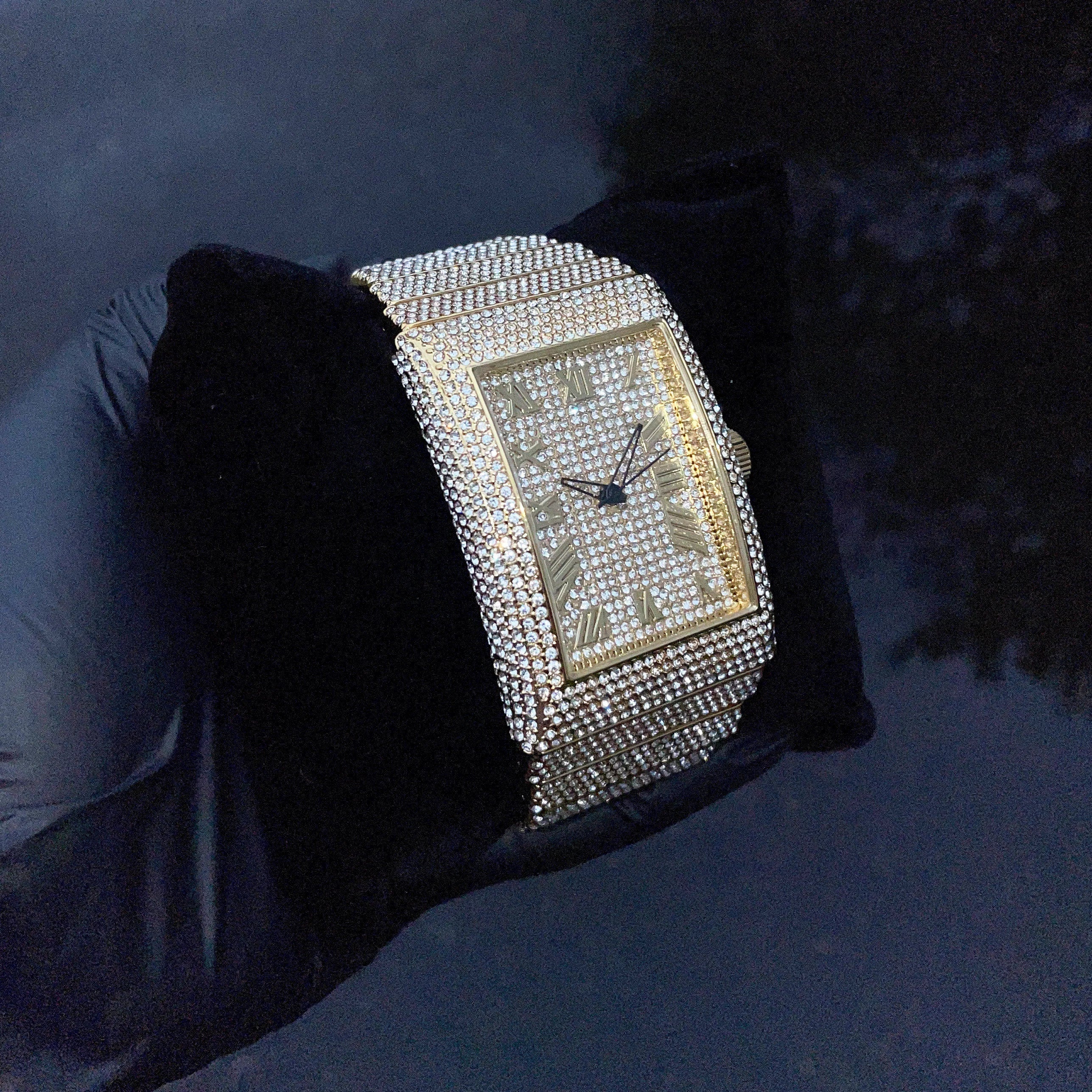 Men's 40mm gold fully iced out diamond watch displayed on black cushion with sparkling stones.
