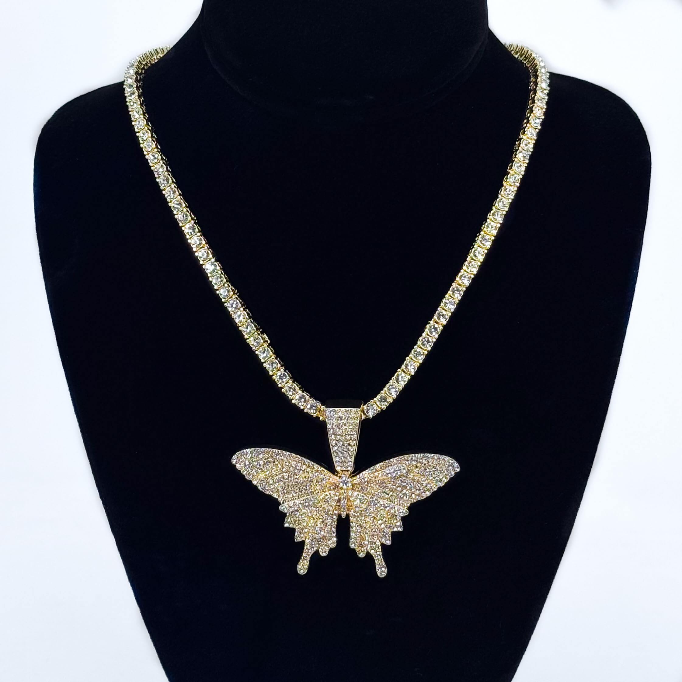 Ladies 60mm iced-out gold butterfly pendant necklace with 4mm tennis chain displayed on stand.