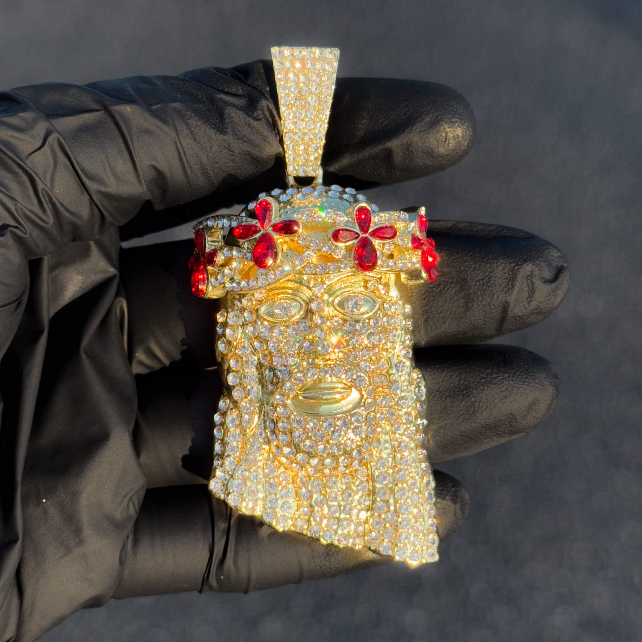 Large gold floral iced-out Jesus pendant with red gemstones, held in glove for detailed view.