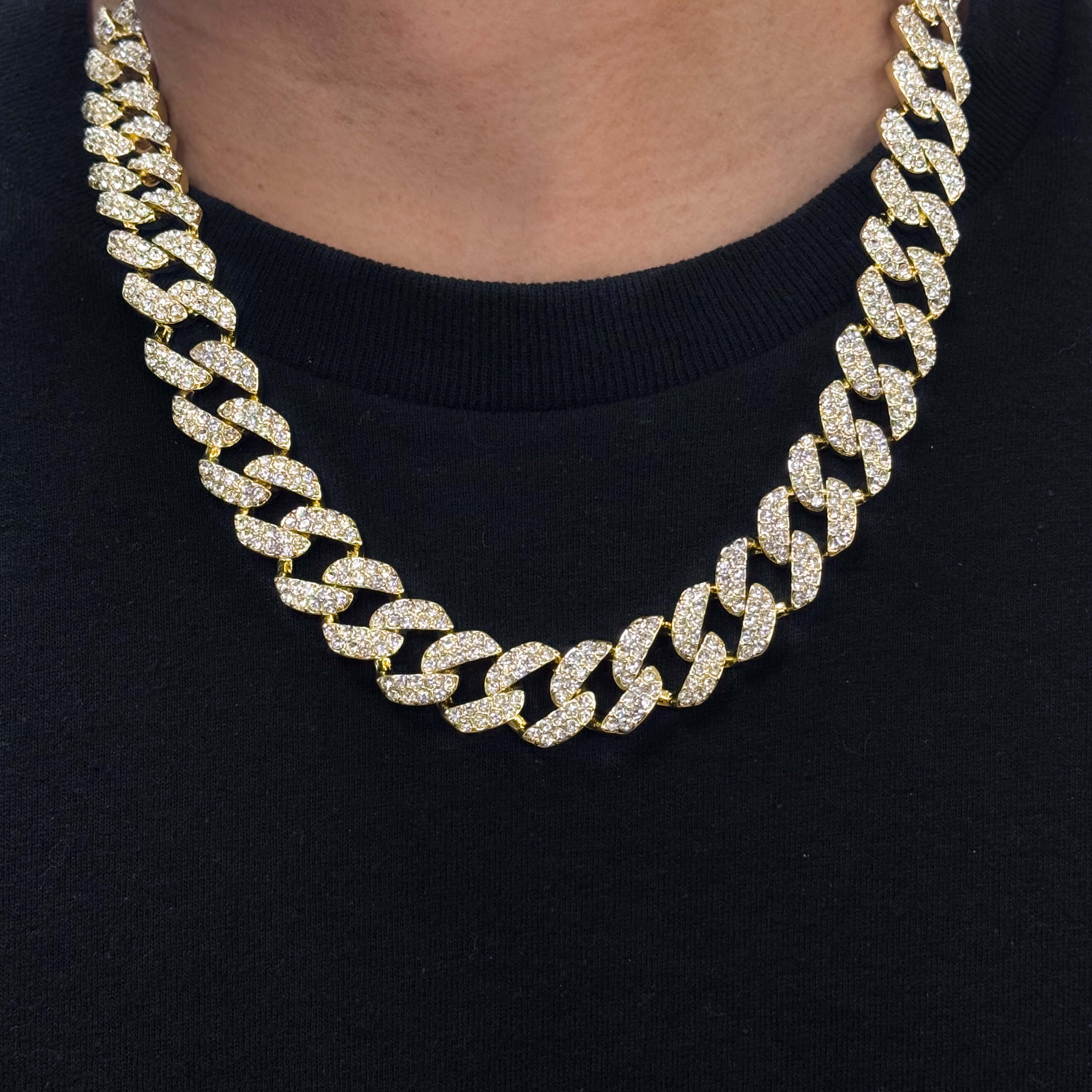 15mm Iced Out Cuban Chain in gold with pavé CZ diamonds, close-up worn on neck over black shirt.
