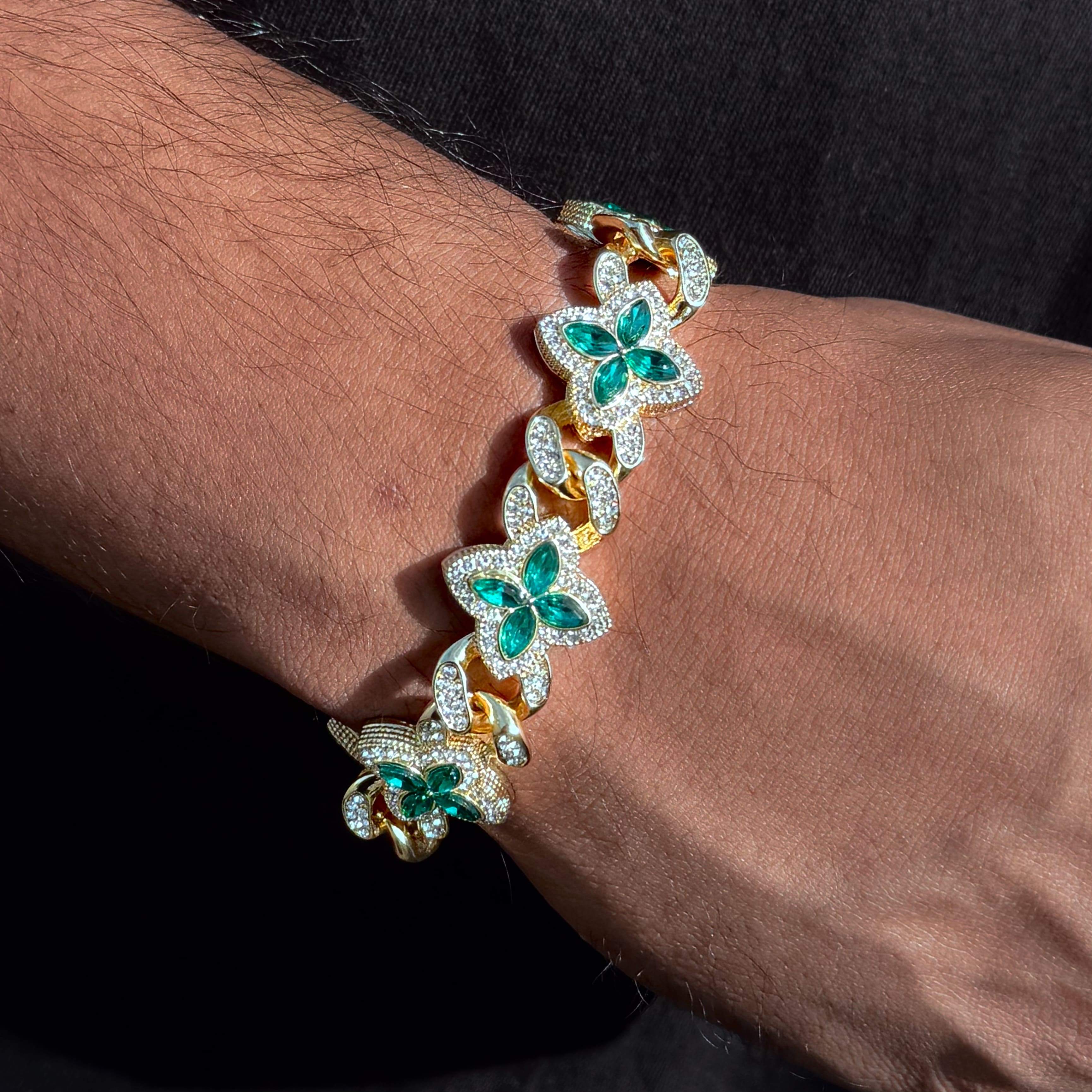 Men’s 20mm Iced Out Clover Link Bracelet in gold with emerald stones shown on wrist