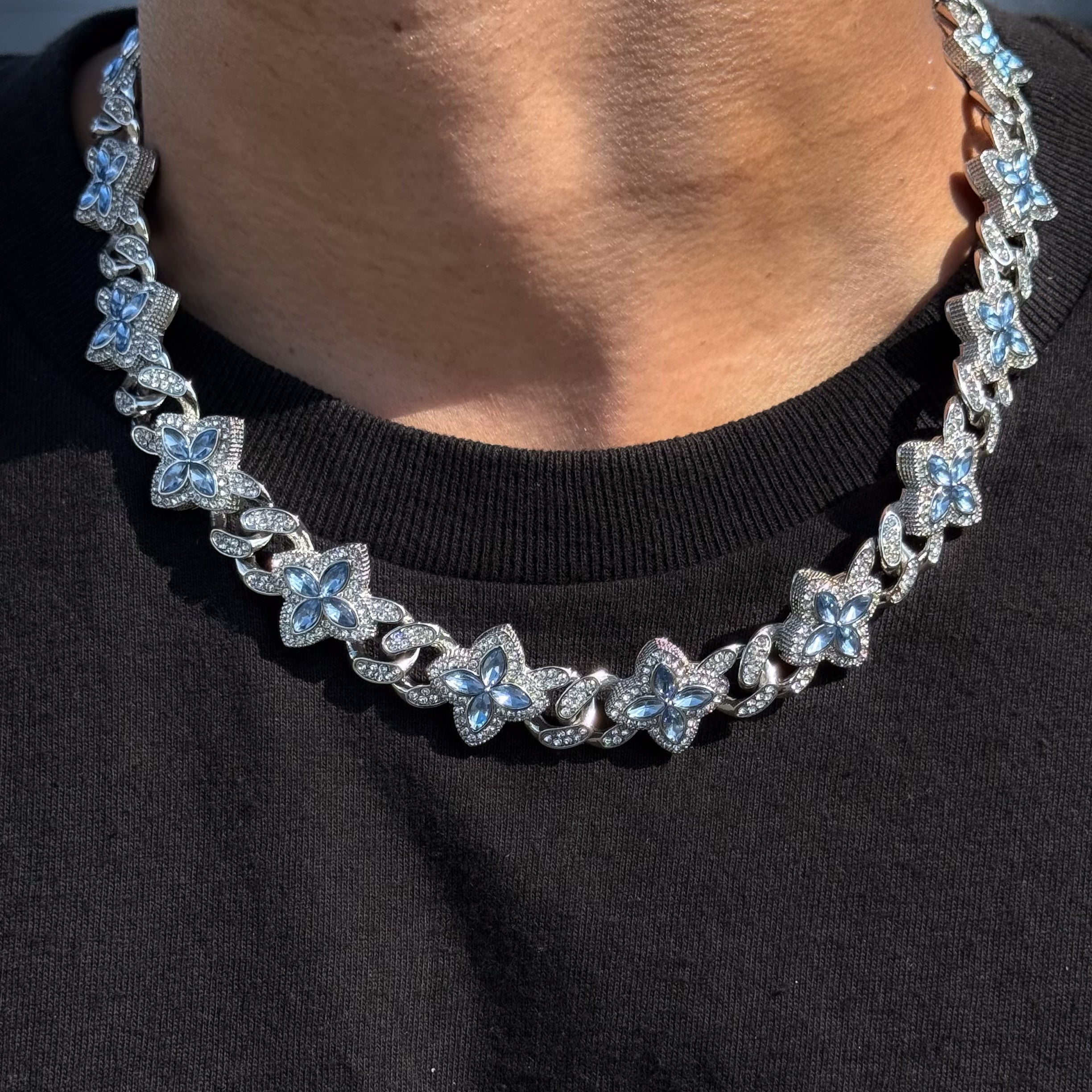 Iced Clover Cuban Chain with blue stones in silver, featuring pavé clover links worn over black shirt.