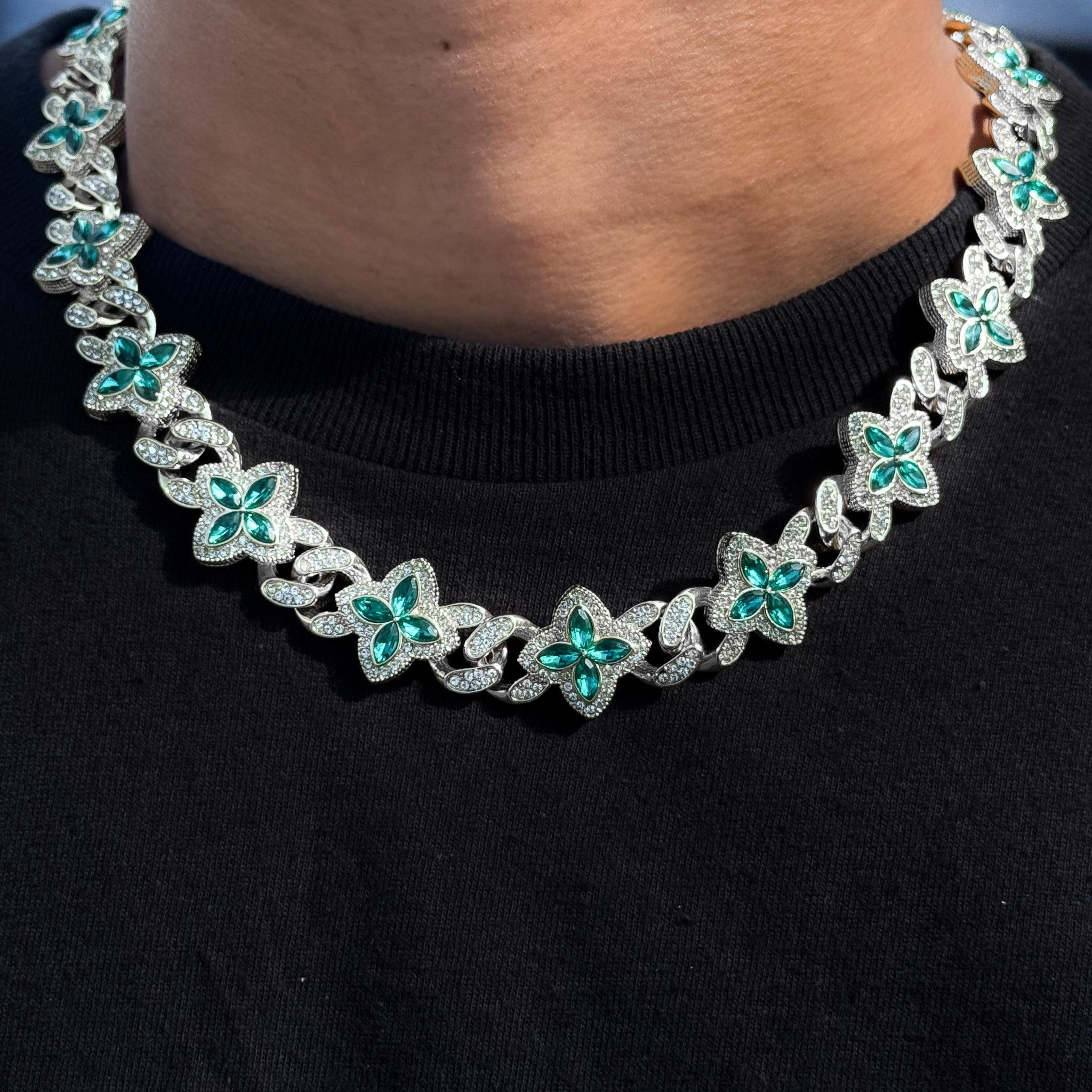 Iced Clover Cuban Chain with green marquise stones on silver links, worn around neck.
