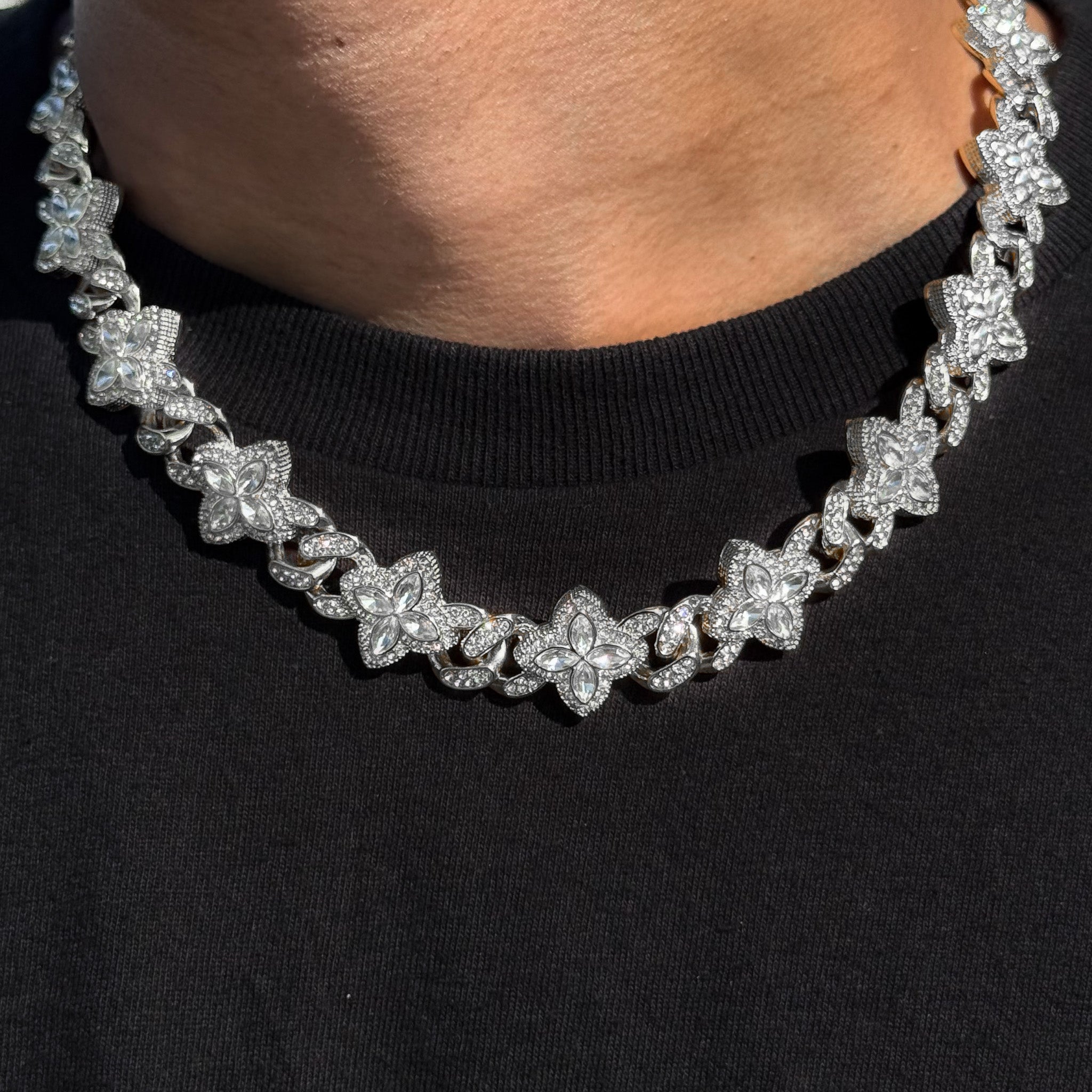 Iced Clover Cuban Chain with clear stones in silver, featuring pavé clover links worn over black shirt.