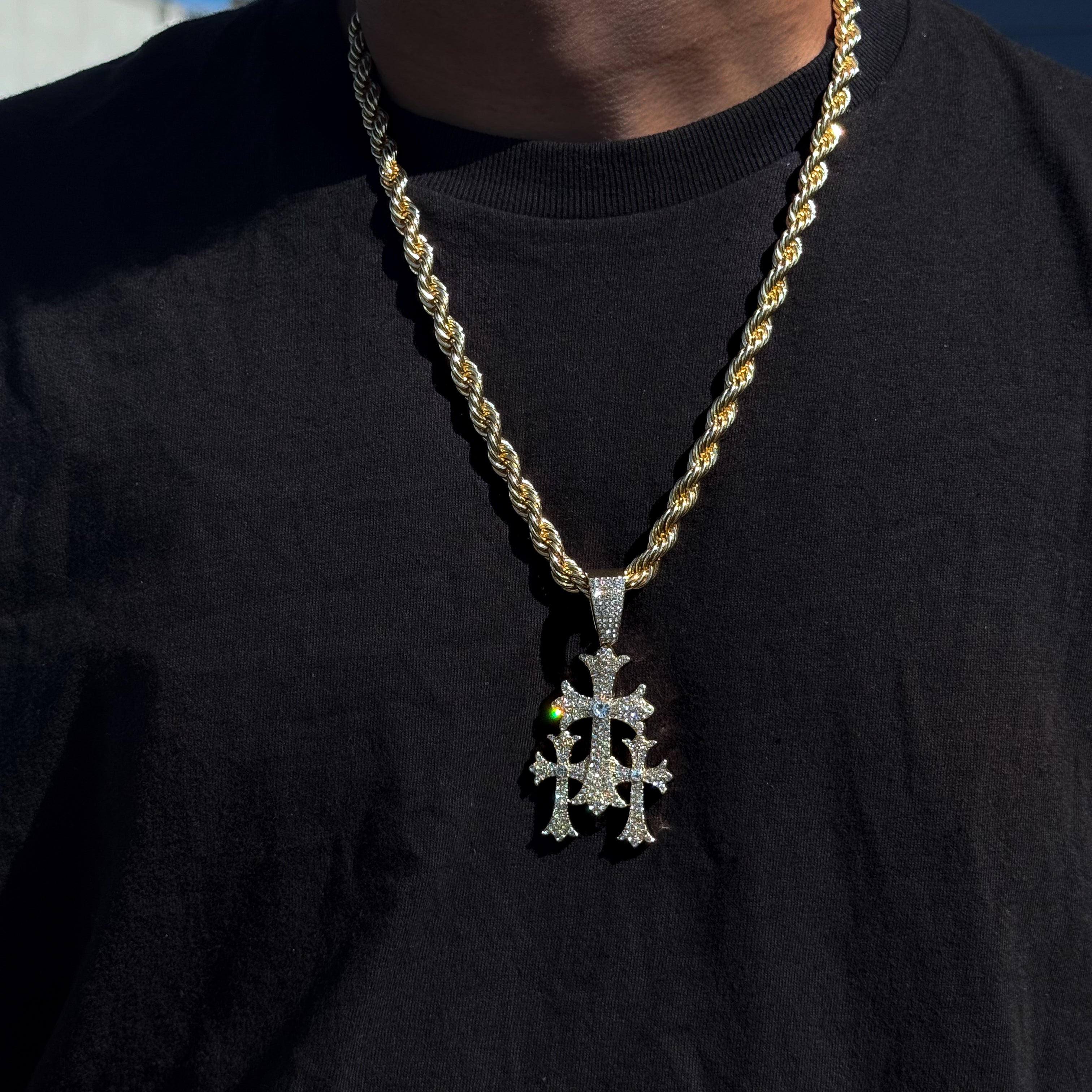 Men’s gold 40mm iced-out cross pendant with 8mm rope chain worn over black shirt outdoors.