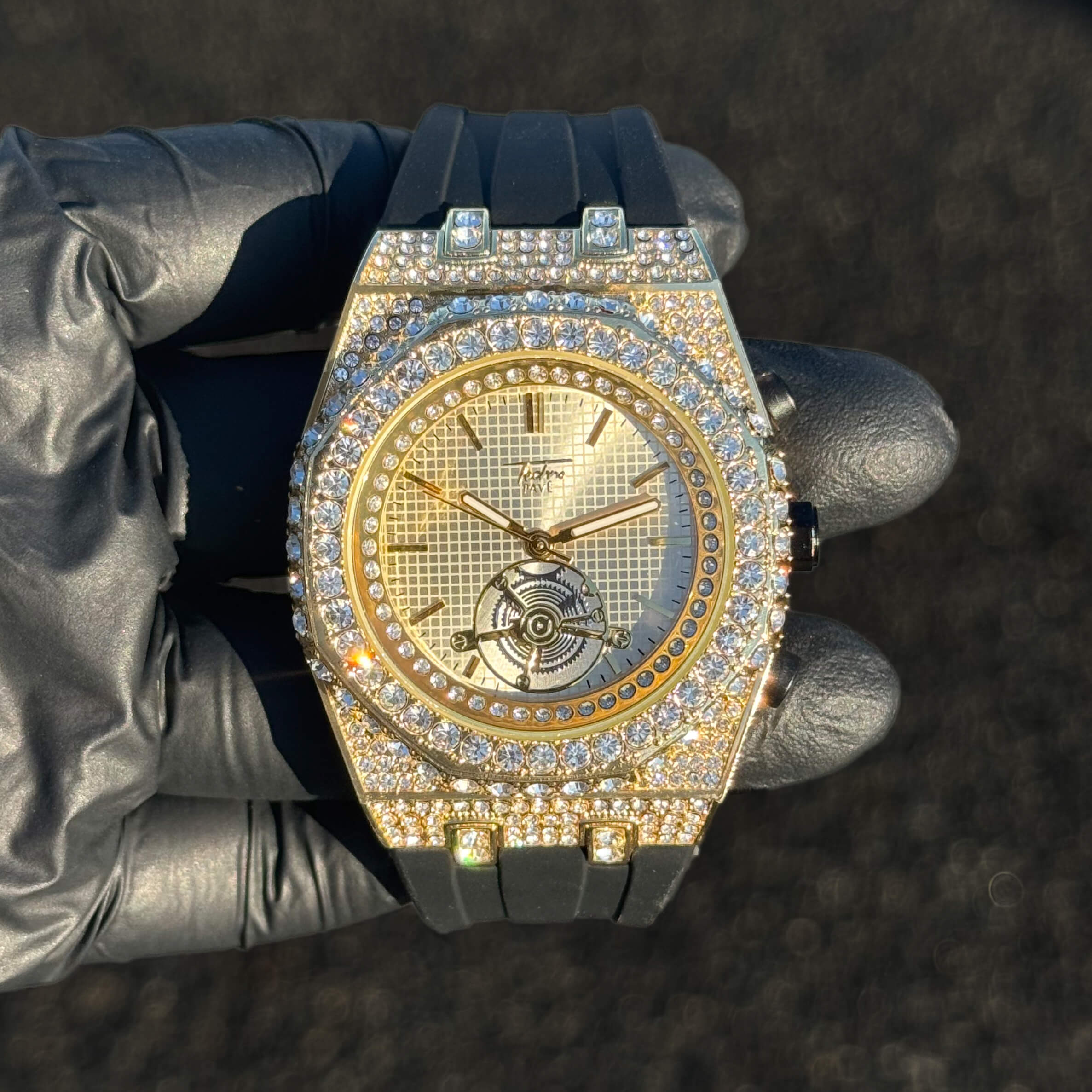 Men's 43mm iced out octagonal case watch with gold dial and black silicone band front view.