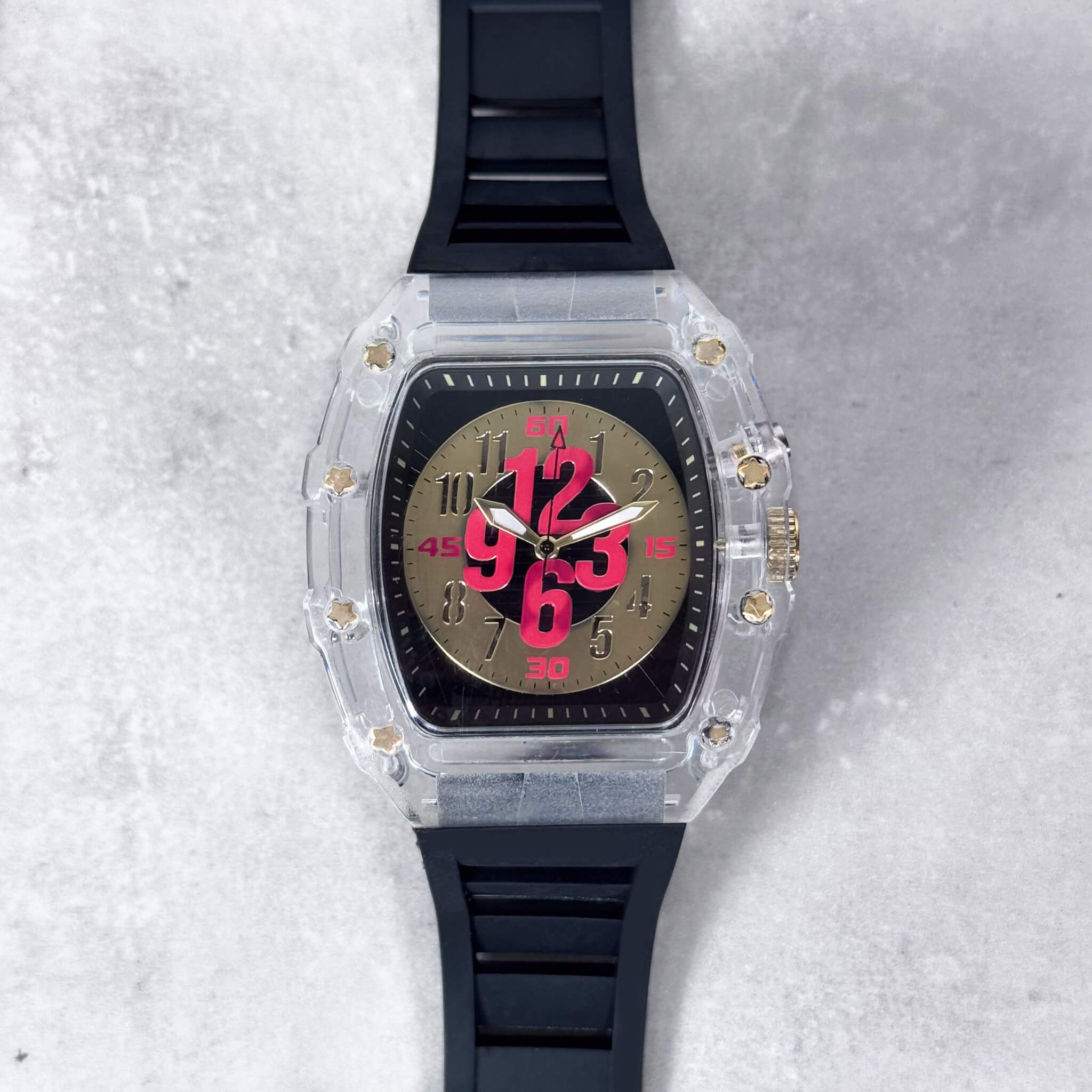 Men's 44mm tonneau watch with clear case, gold dial and bold red numbers, black silicone band.